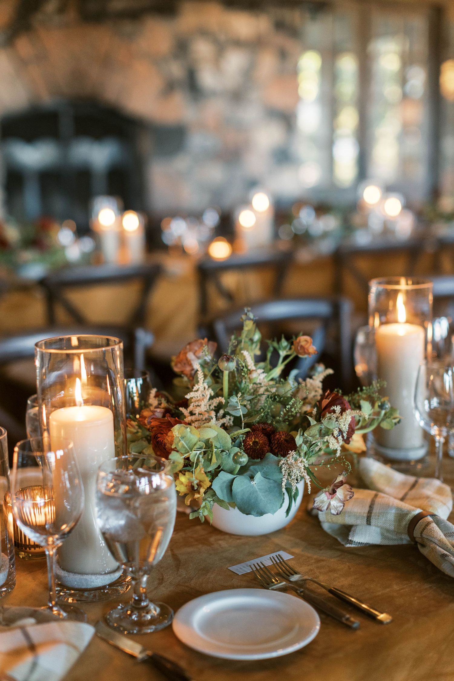 Romantic table setting with glowing candles and greenery centerpiece on wooden farmhouse table.