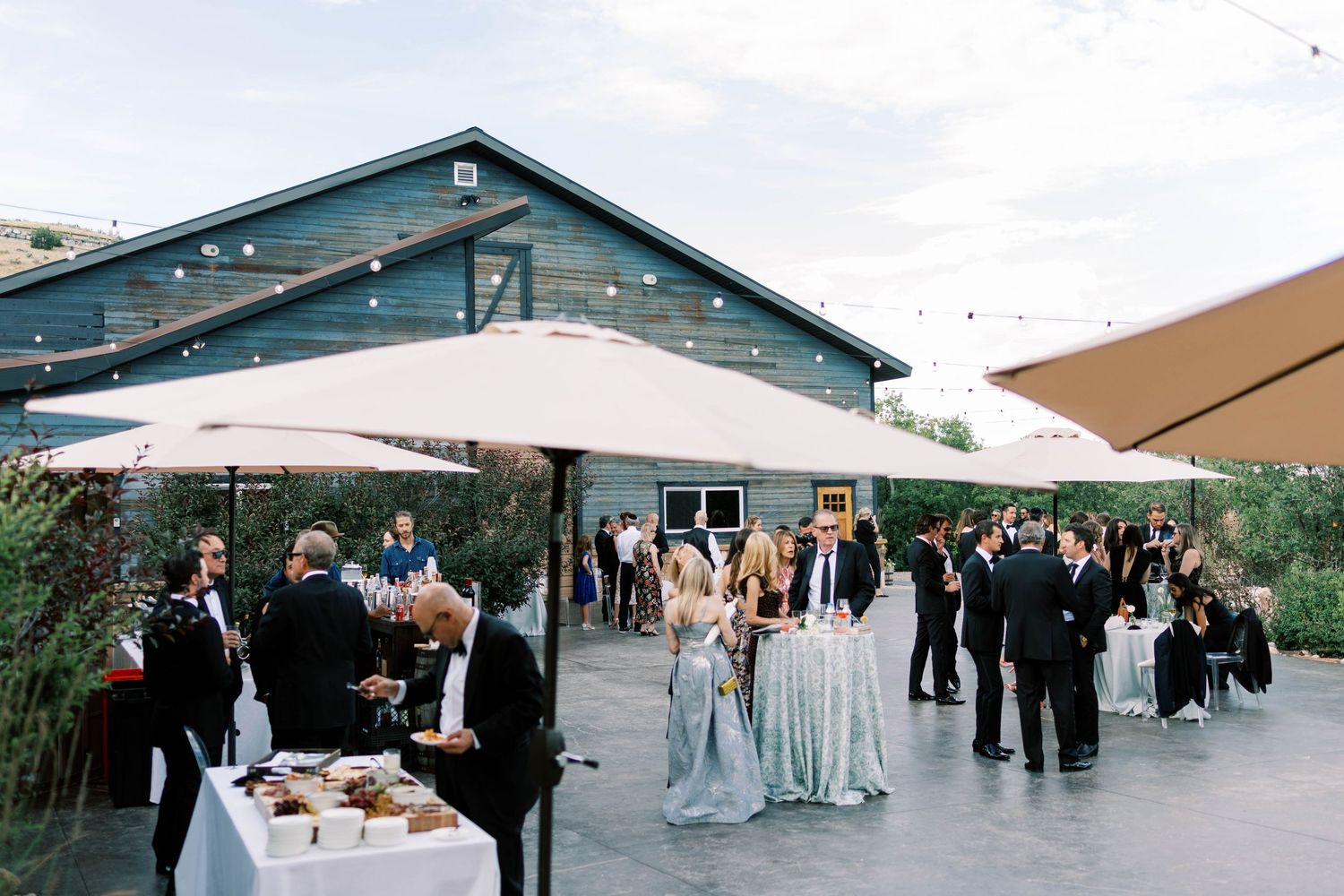 Outdoor wedding reception at blue sky ranch with guests mingling under string lights and umbrellas.