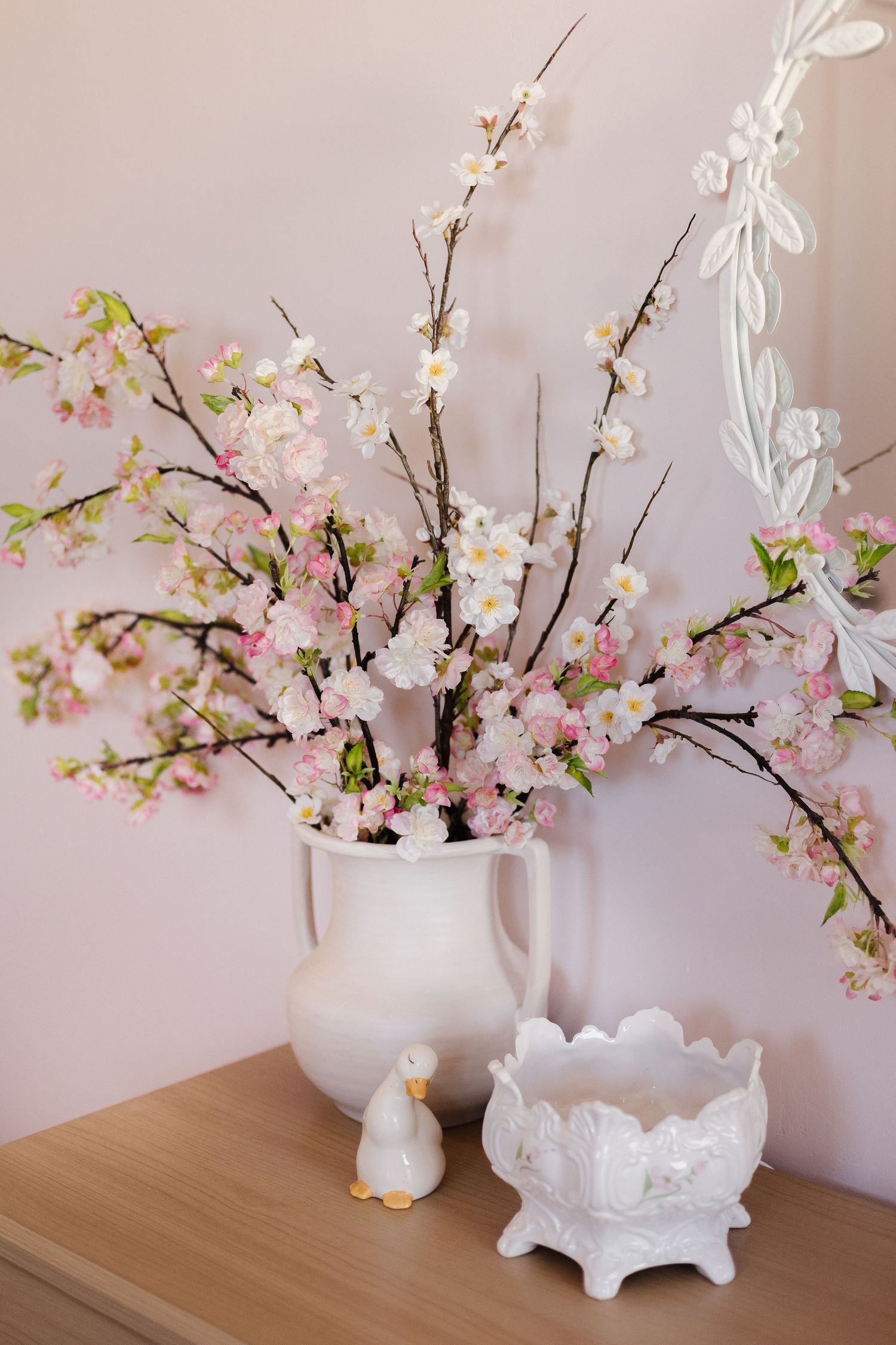 Cherry blossom branches arranged in a white ceramic vase with decorative white pottery accessories.