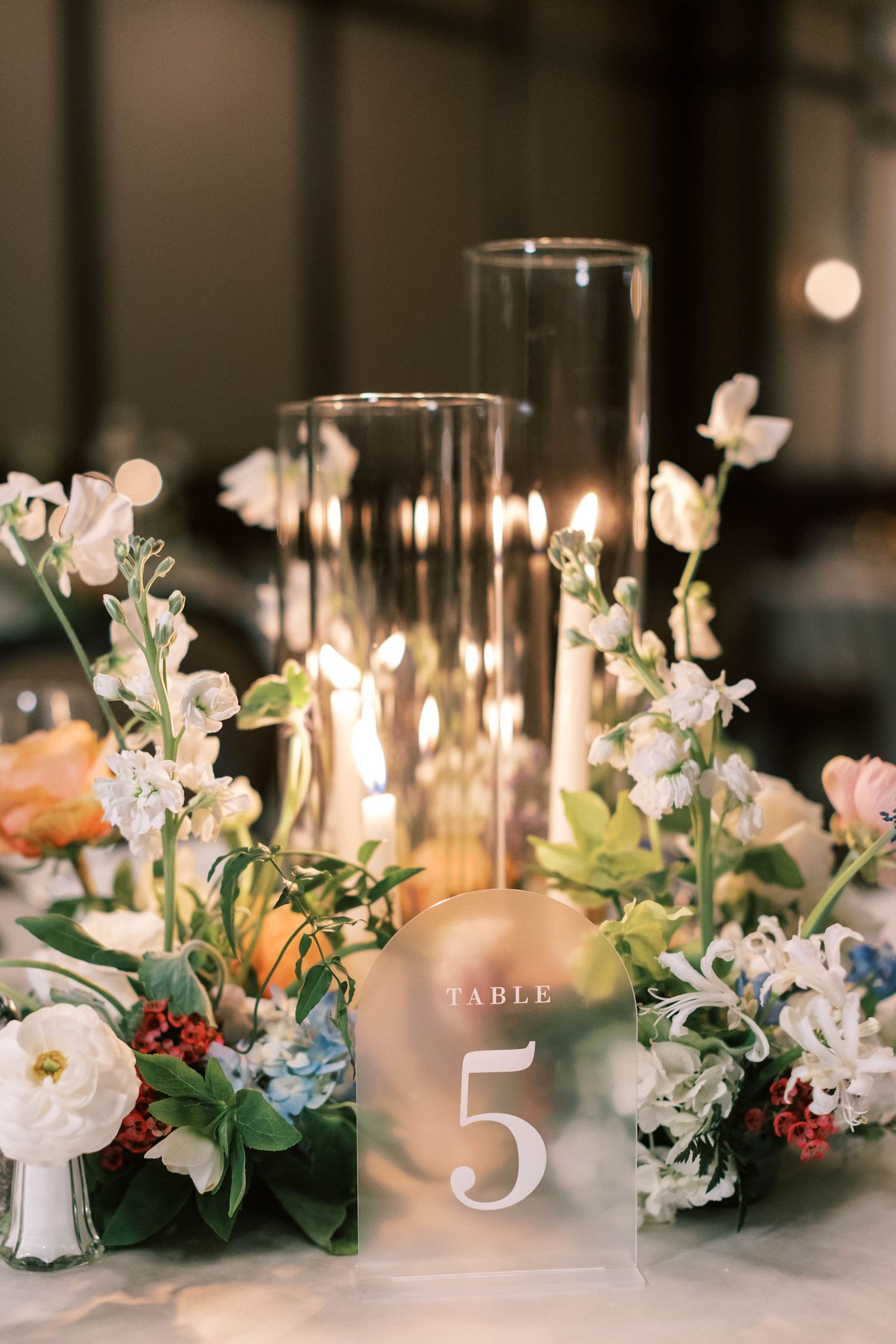 Elegant table centerpiece with glass hurricane candle holders and table number 5.