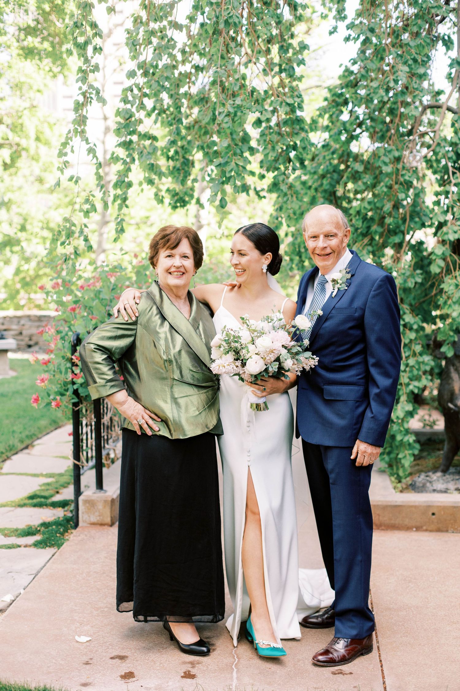 Wedding party poses for formal portrait in lush garden setting with stone pathway.