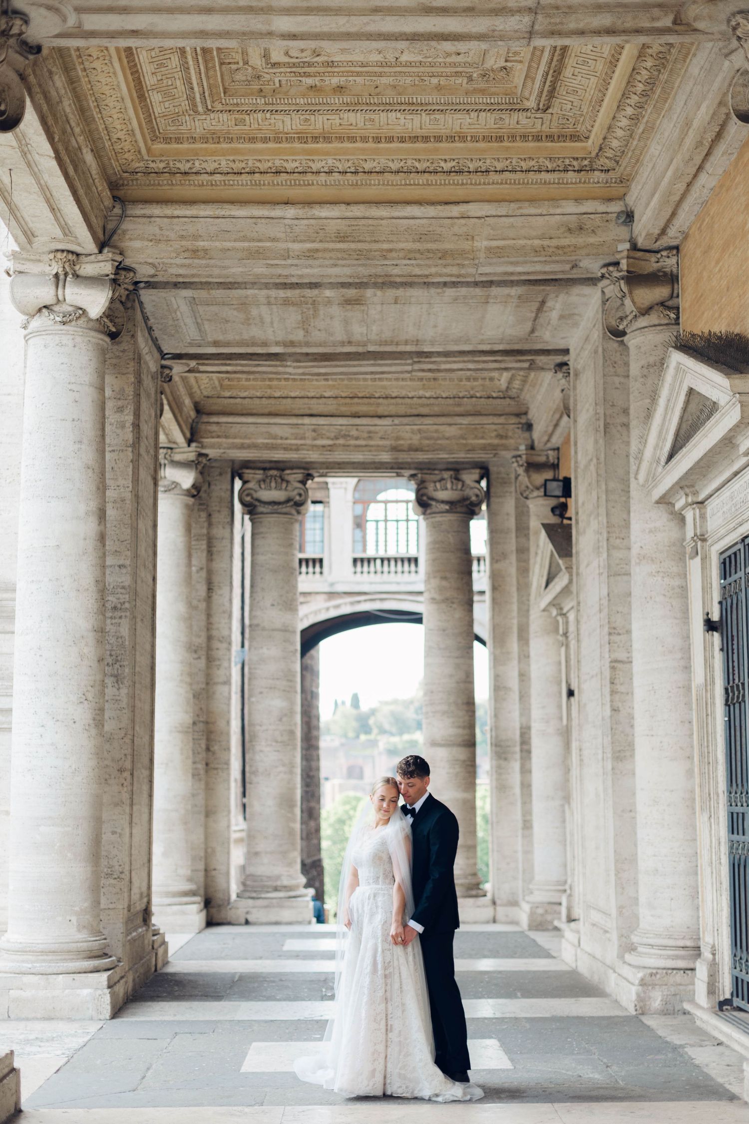 A wedding couple stands in an elegant colonnade with ornate classical architecture and stone pillars of rome italy.