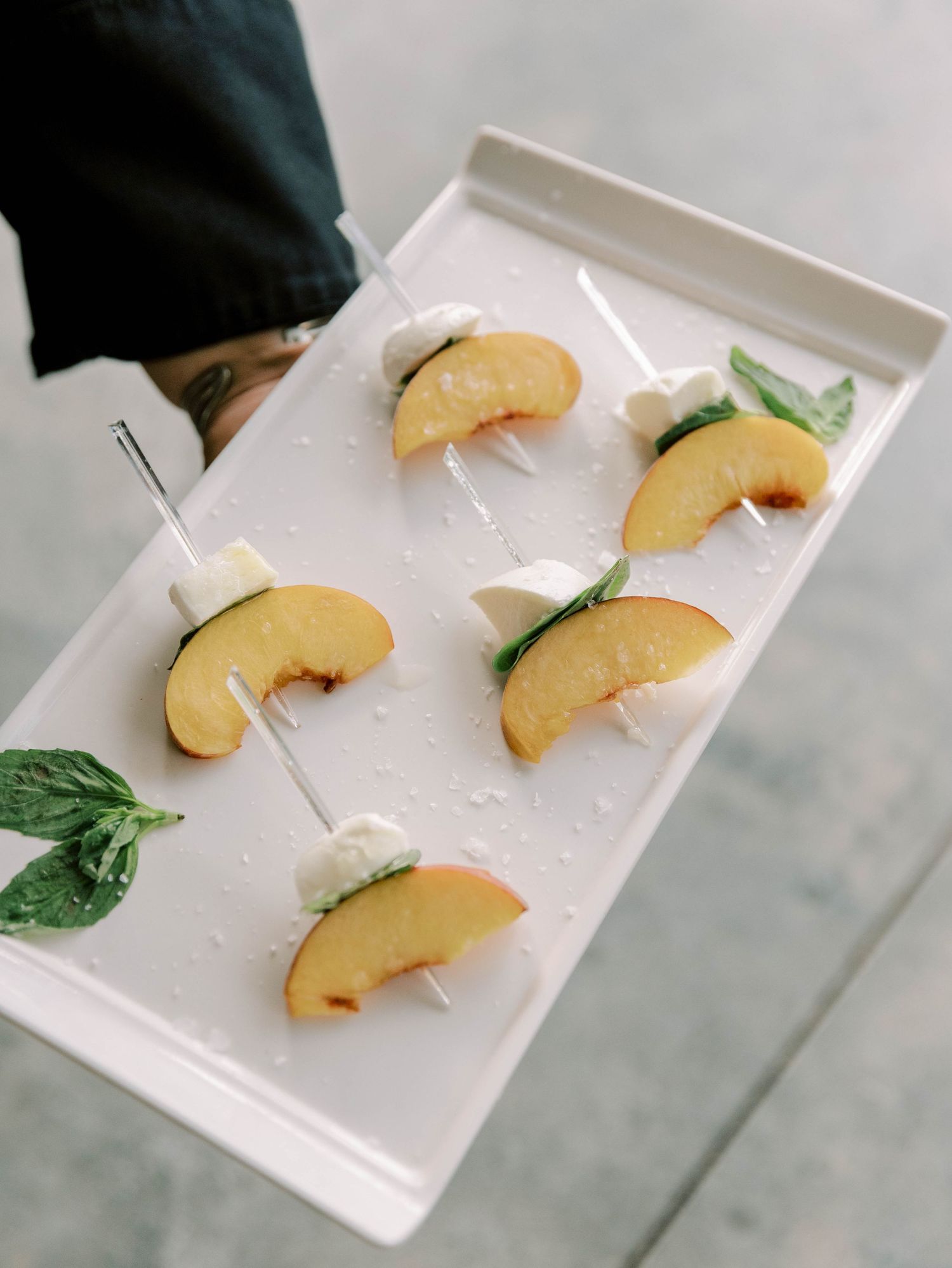 Elegant appetizer of peach slices garnished with herbs served on a white platter.