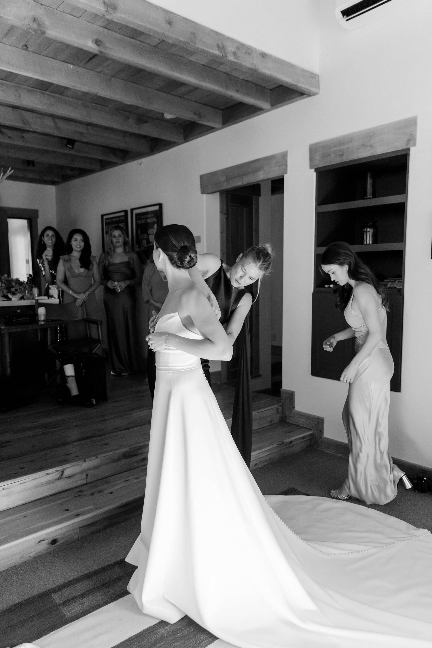 Black and white photo of wedding dress preparations with attendants helping.