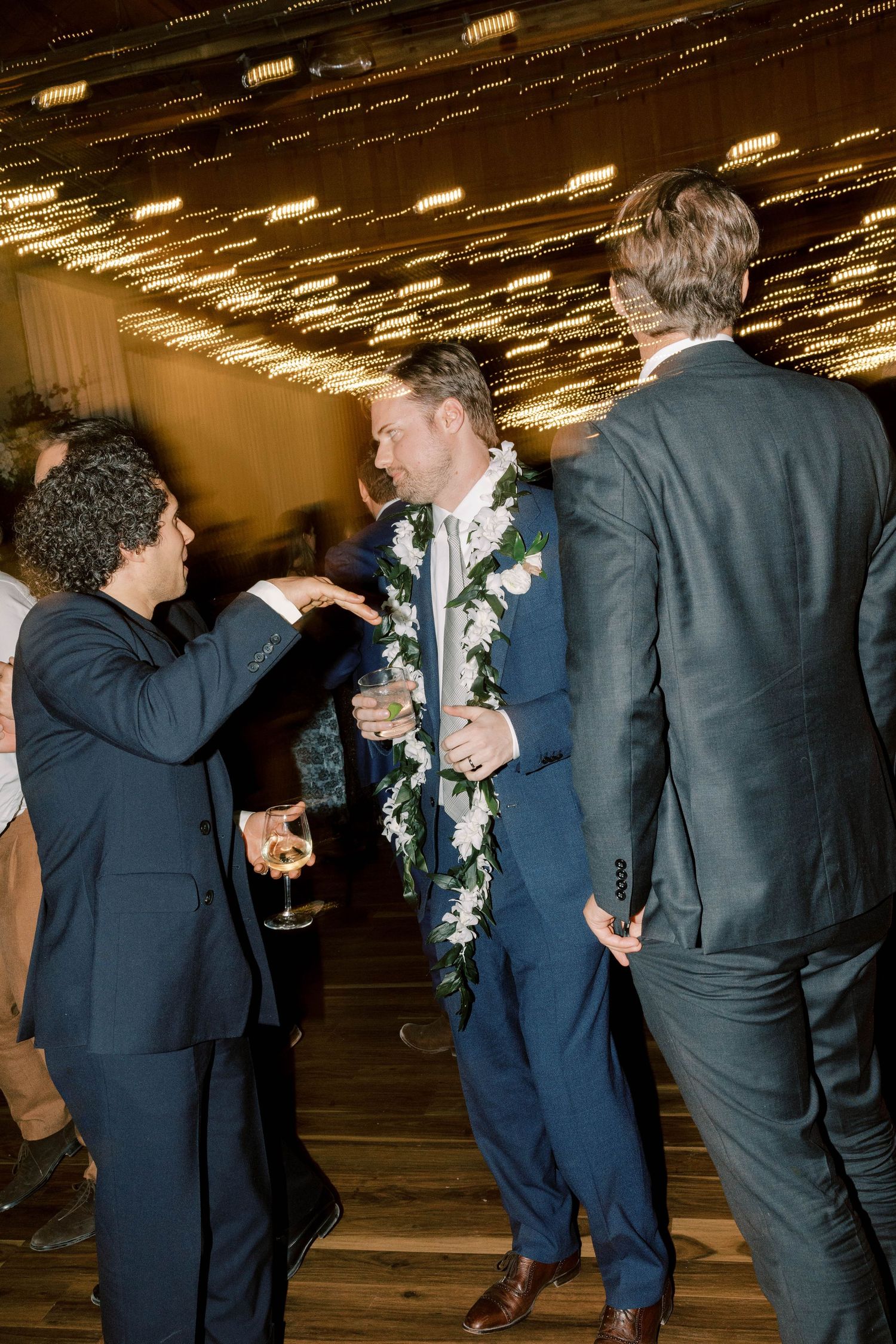Wedding guests dancing and celebrating under decorative ceiling lights.