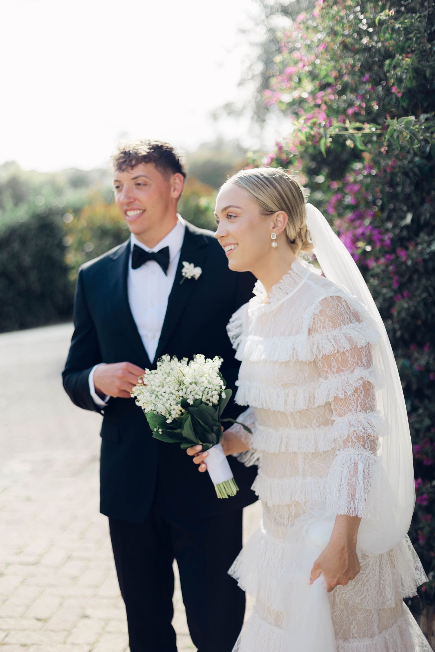 Candid wedding moment captured on stone path with blooming flowers in background.