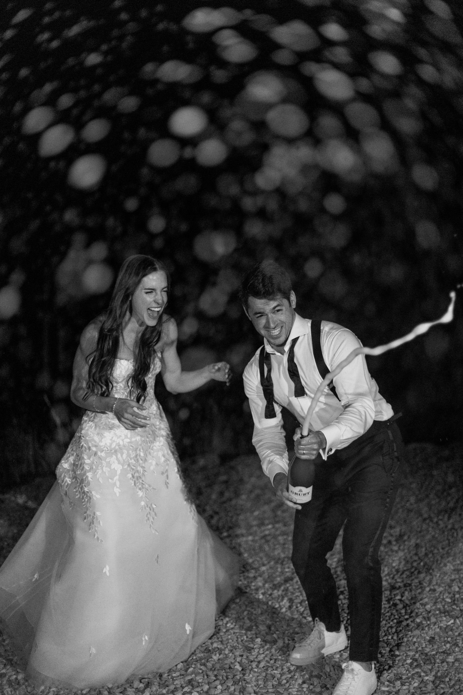 Couple laughing and dancing with champagne at nighttime wedding celebration.