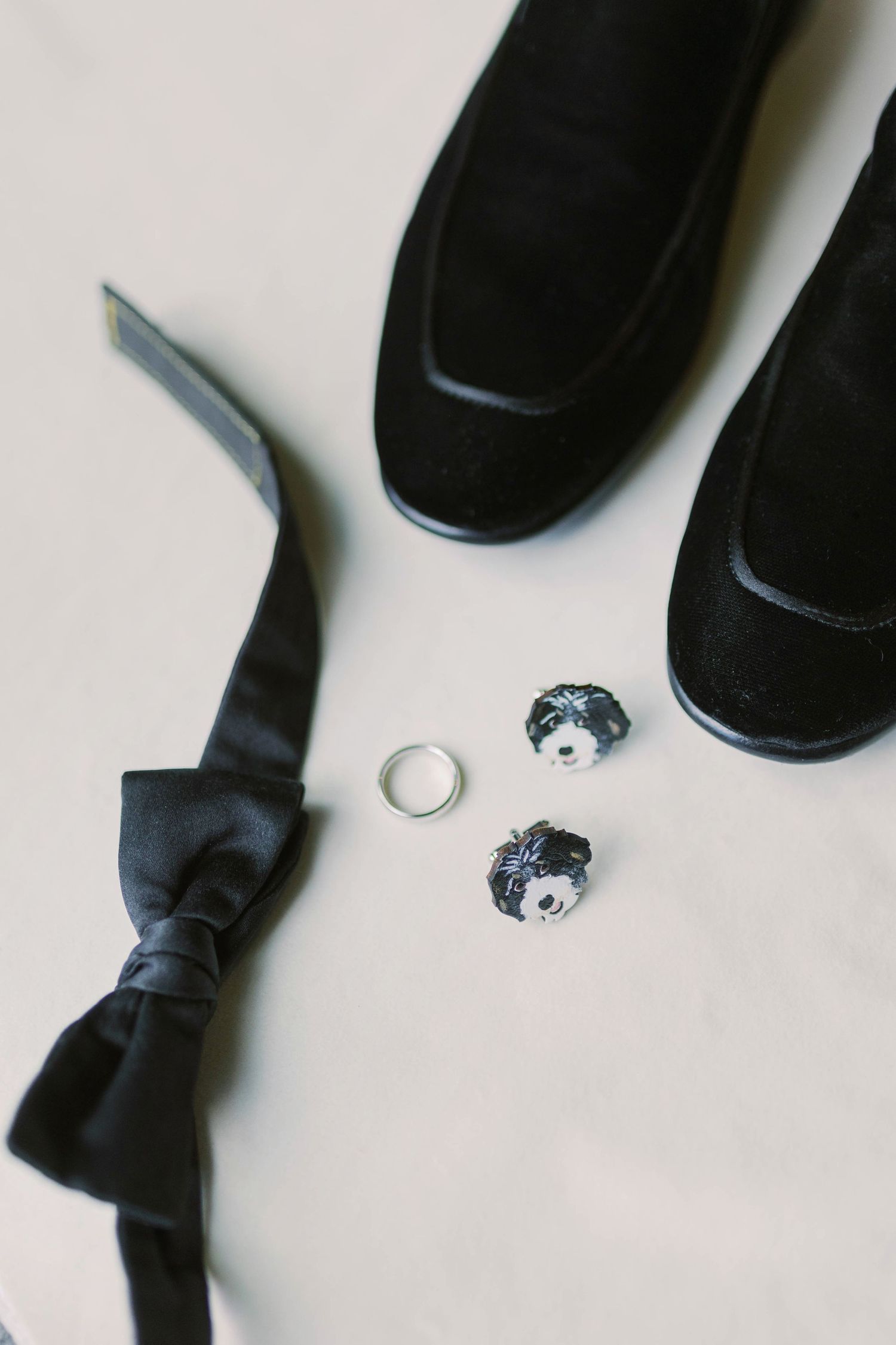 Black formal bow tie and dress shoes with crystal cufflinks on light beige background.
