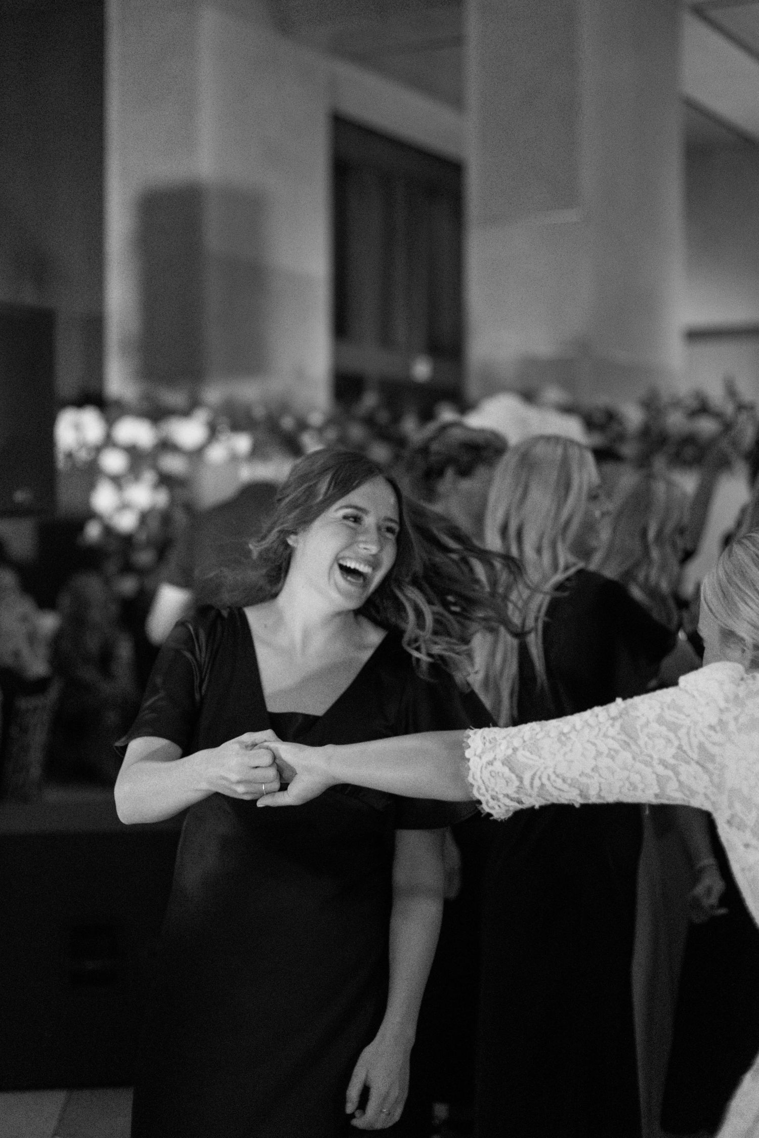 Black and white photo of joyful dancing at a wedding reception with guests in formal attire.