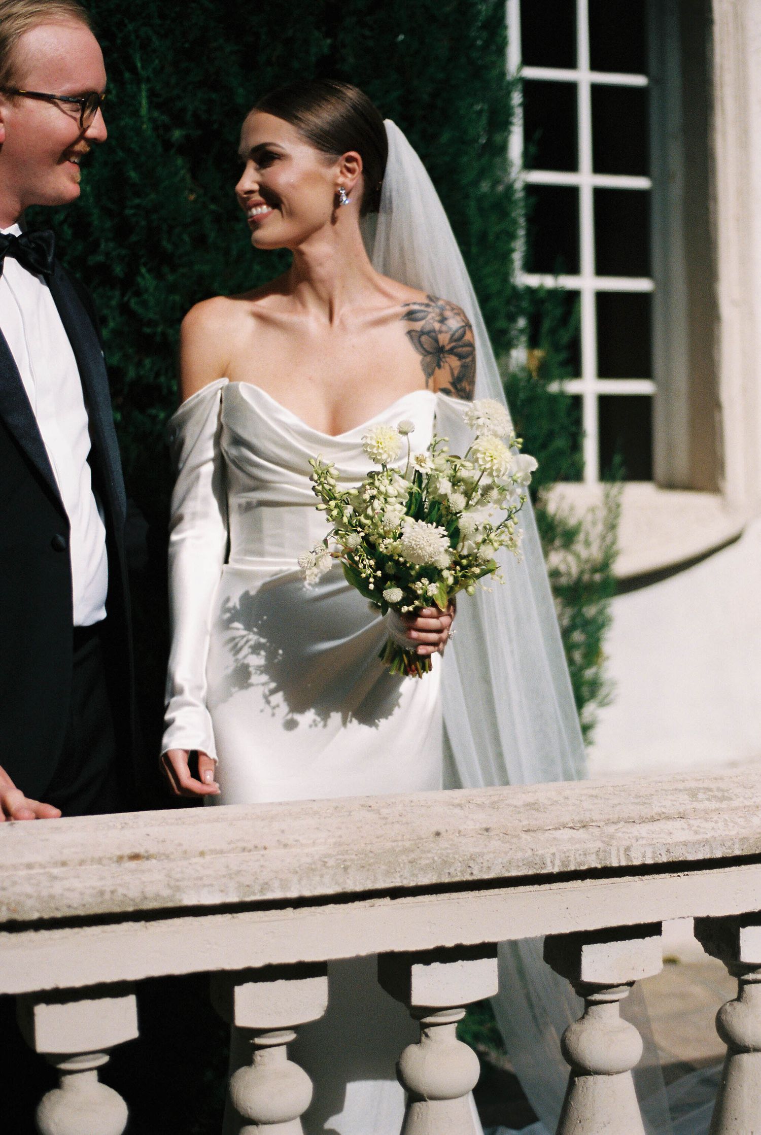 Wedding couple sharing a joyful moment on stone balcony of elegant mansion.