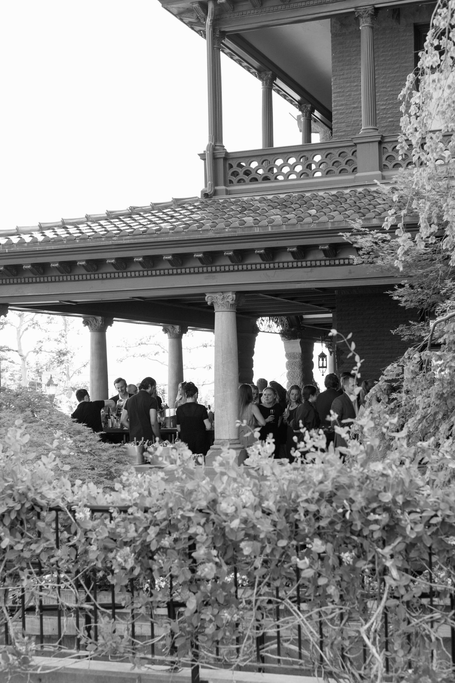 Black and white image of guests gathered on an ornate covered porch of a historic building.