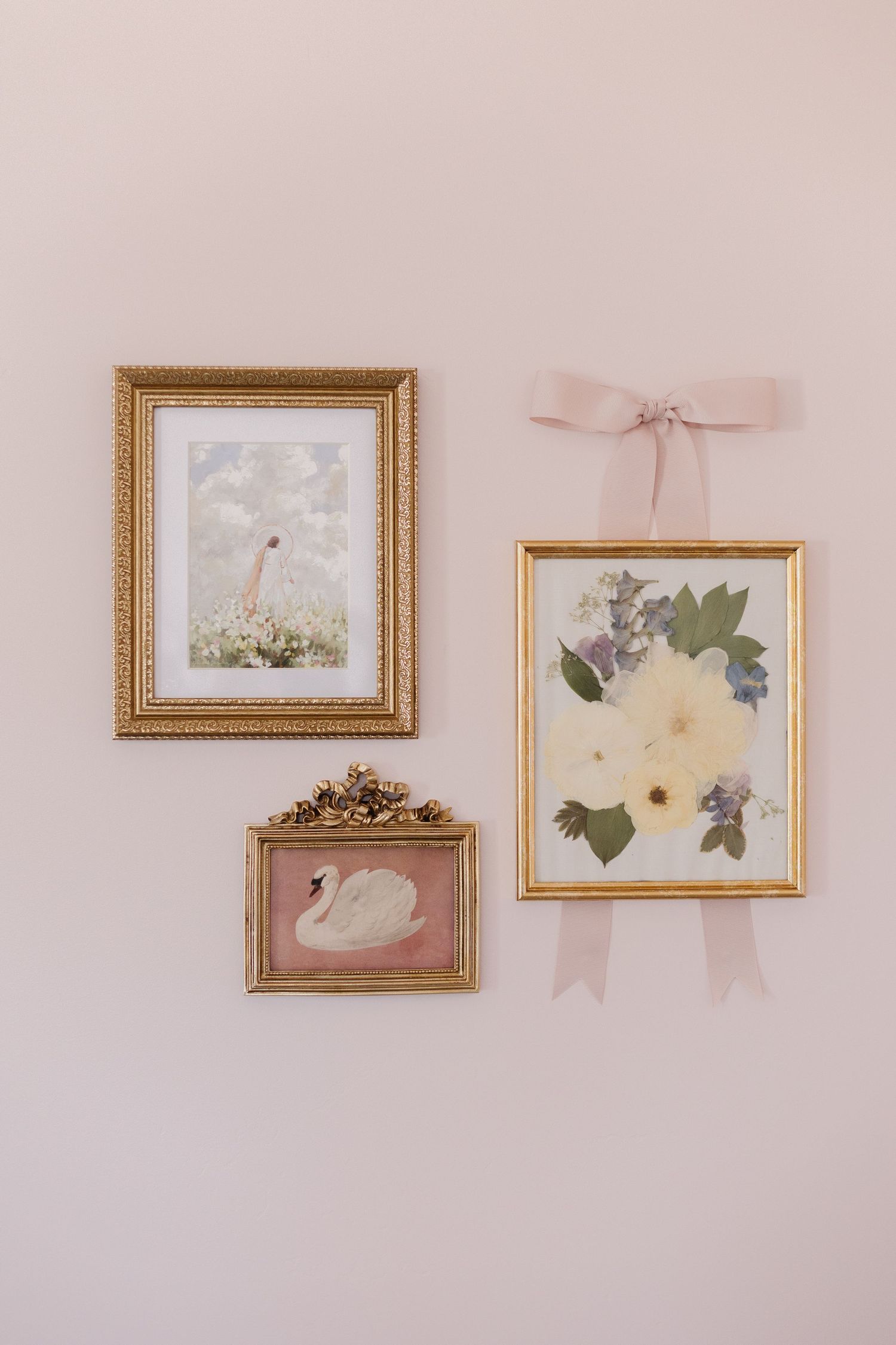 Three vintage-style framed artworks featuring a swan, floral arrangement and lighthouse hang on a pink wall with delicate bows.
