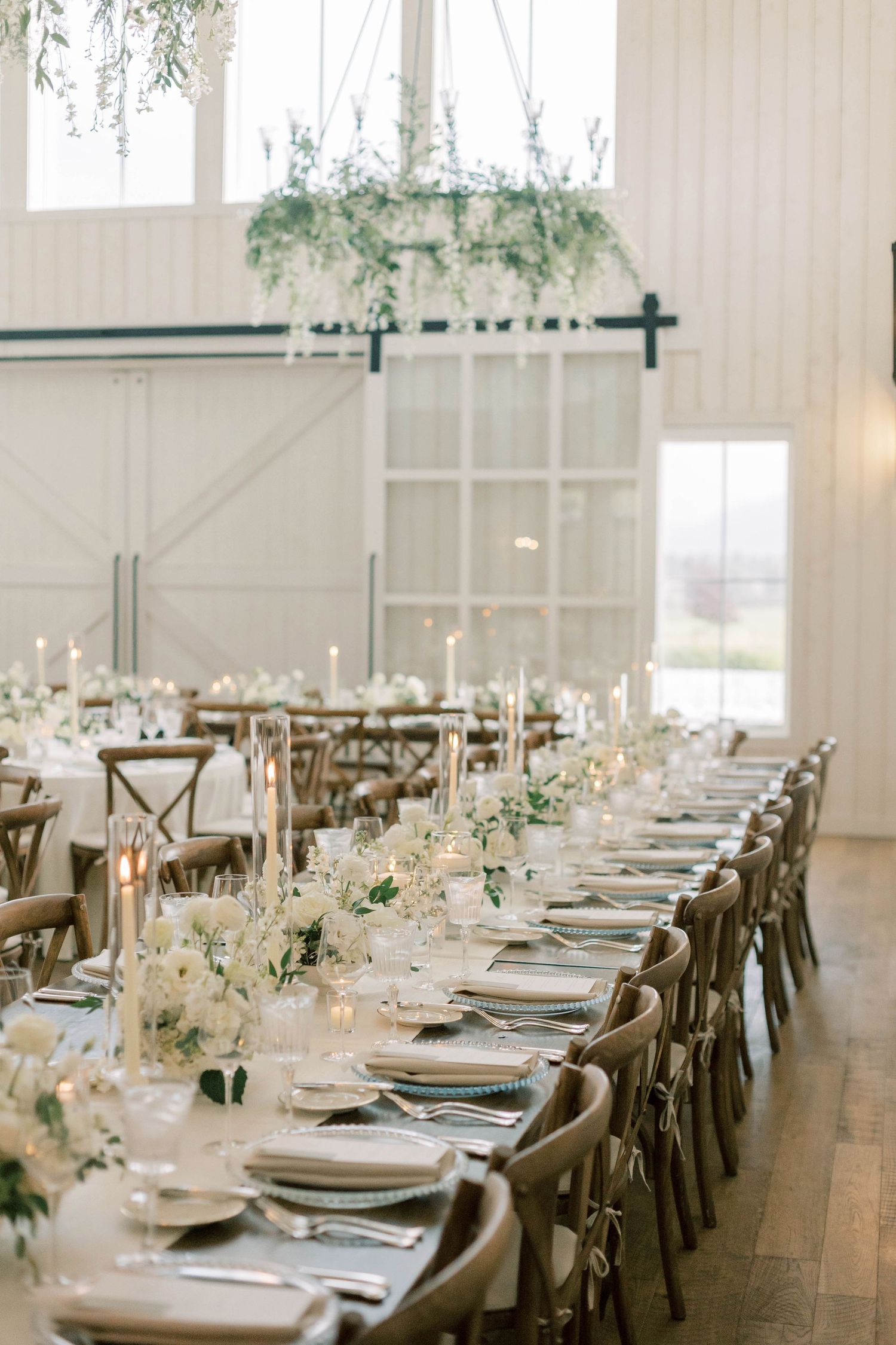 Long banquet table set with elegant place settings and suspended greenery decor.