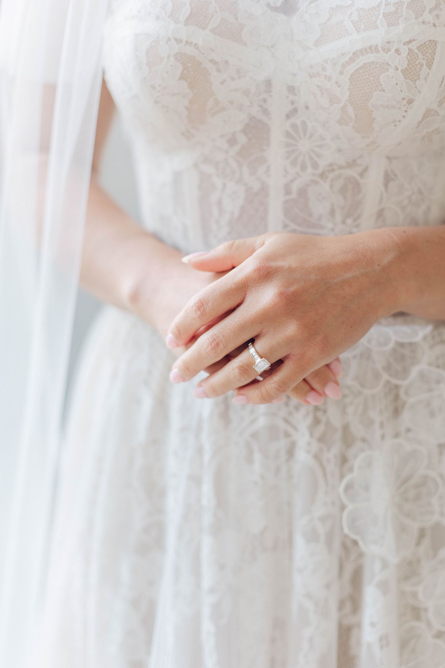 Close-up of a delicate diamond wedding ring on a hand against white lace fabric.