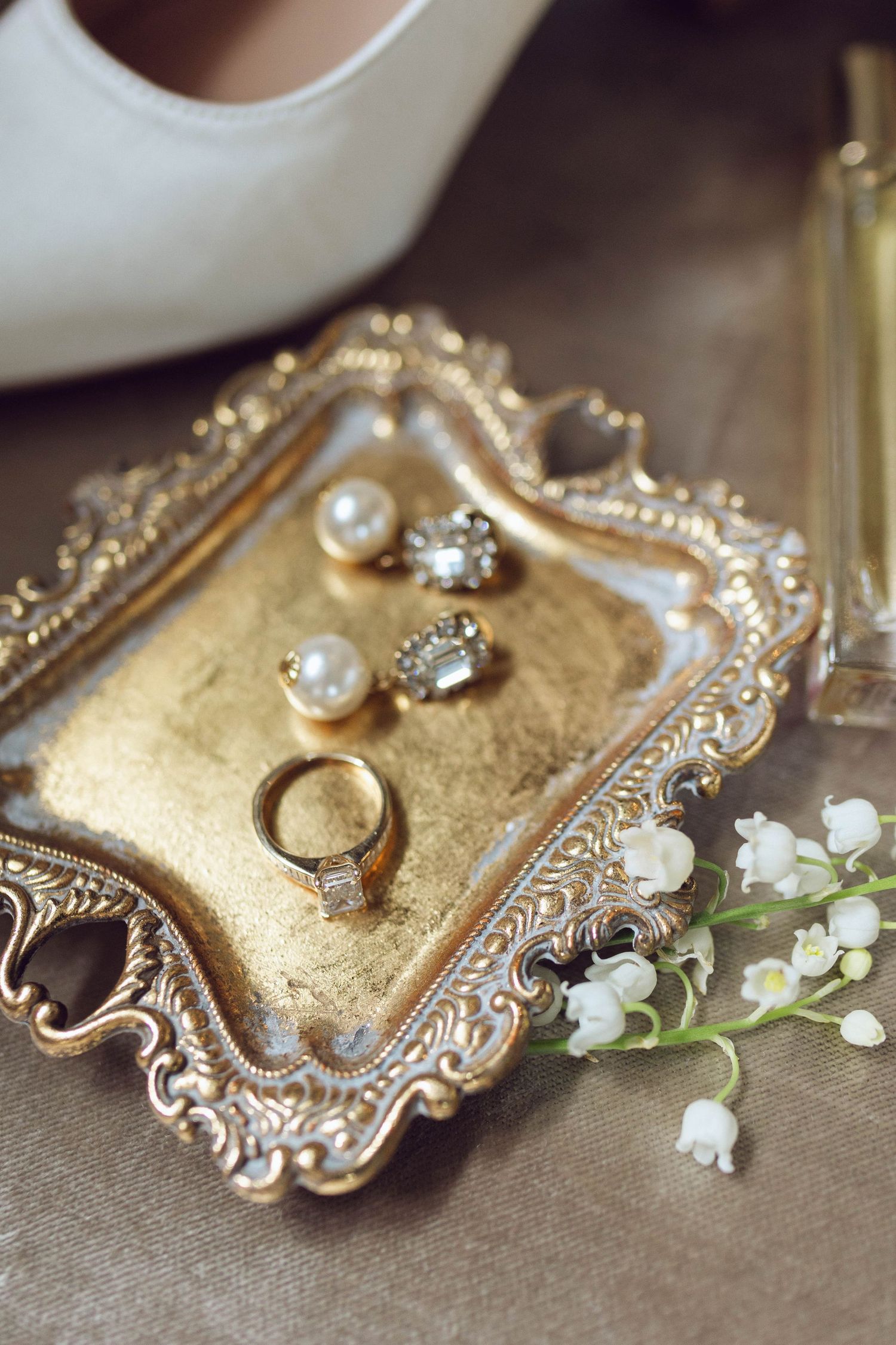 Wedding jewelry and rings displayed on vintage gold decorative tray with lily of the valley flowers.