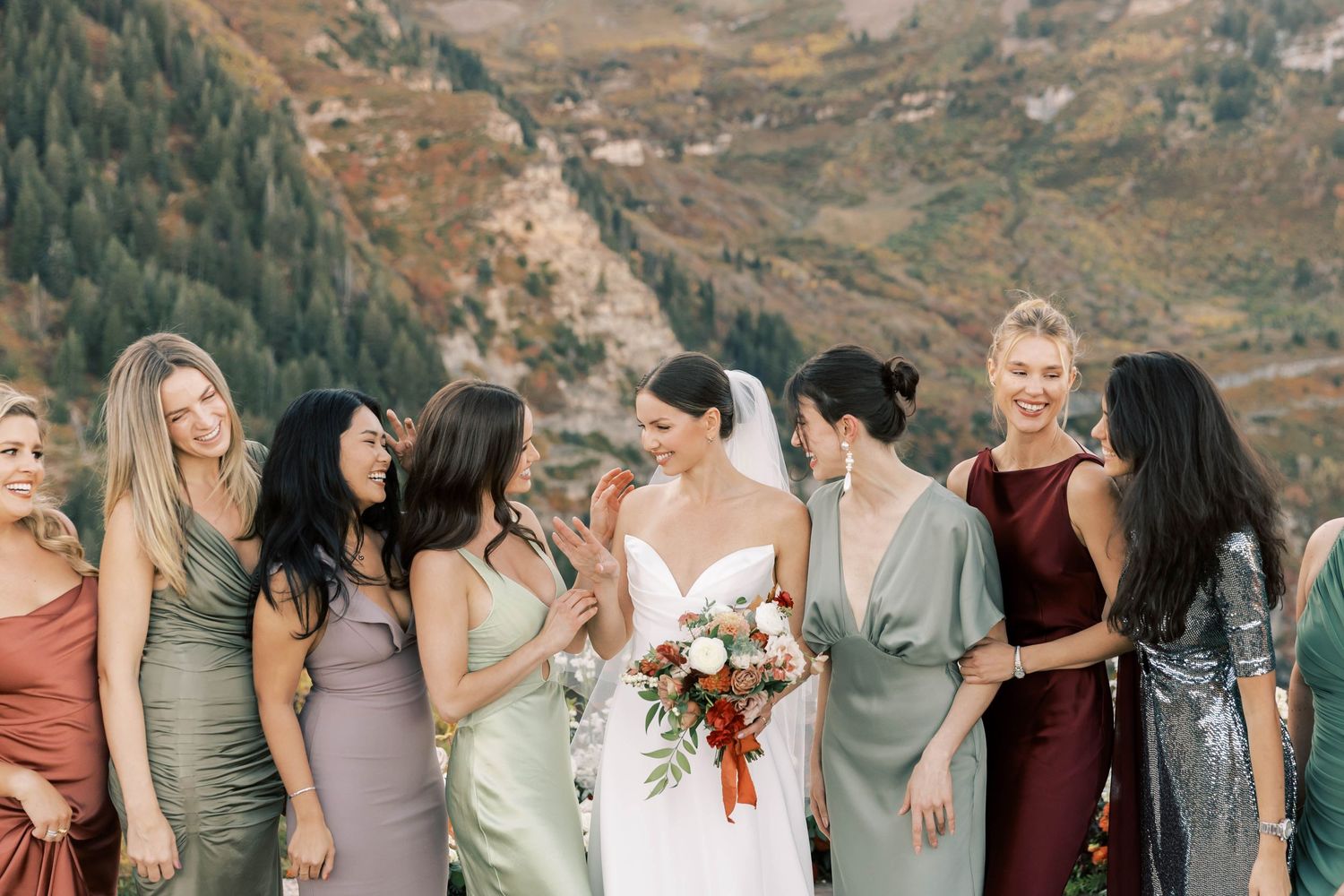 Wedding party in jewel-toned dresses gathered for photos with mountain scenery.