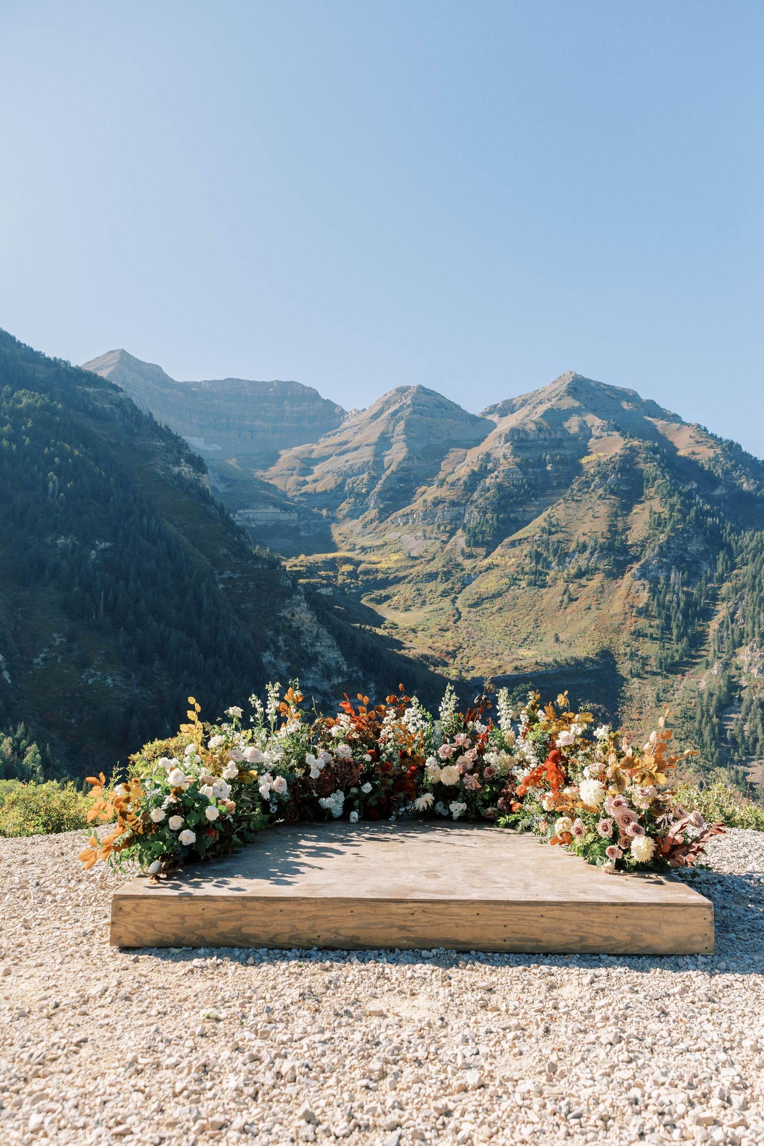 Mountain wedding ceremony arch adorned with autumn flowers against dramatic mountain peaks in the background.