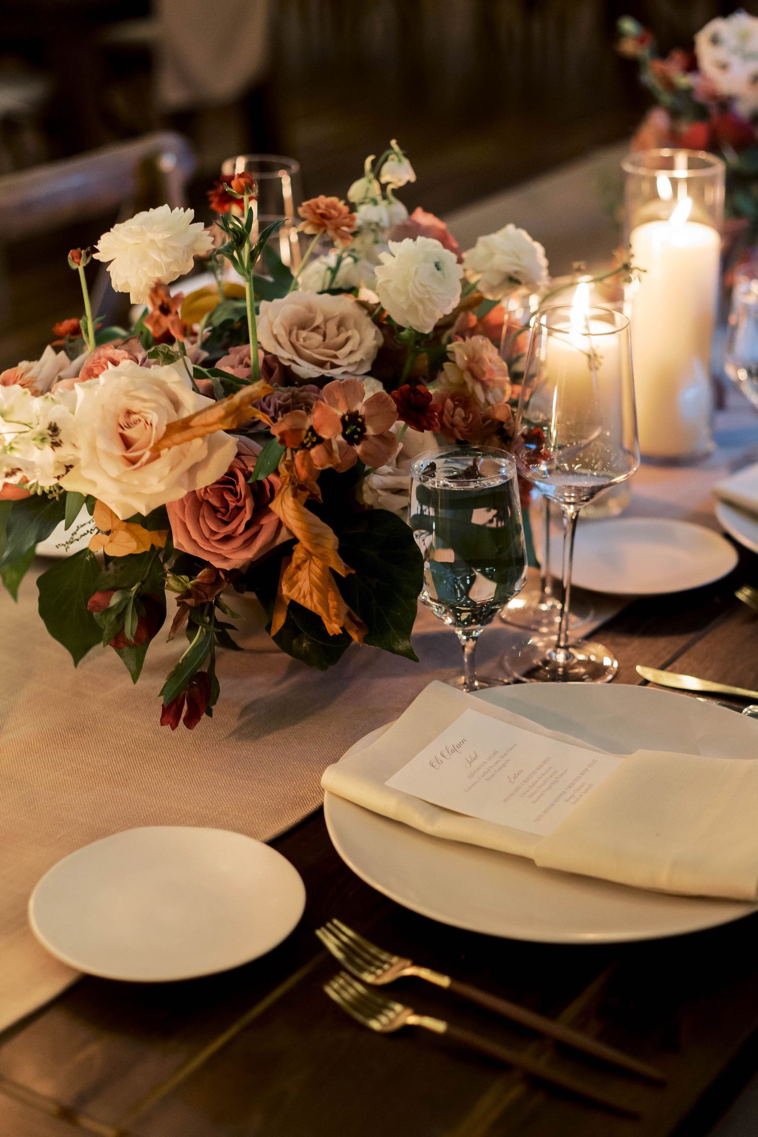 Romantic table setting with blush roses, candles, and elegant place settings for a wedding reception.