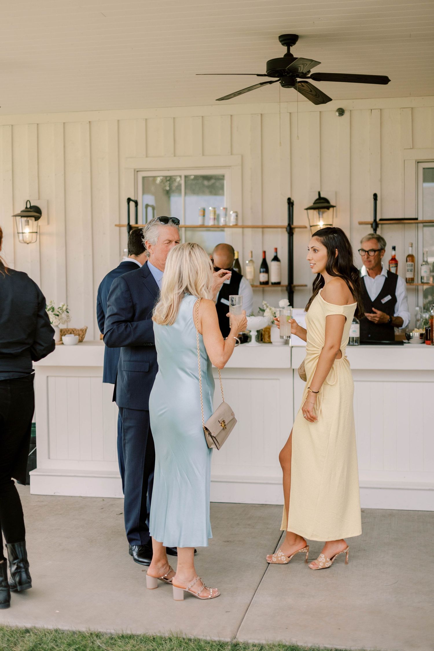 Guests mingling at an elegant white indoor bar with pendant lighting.