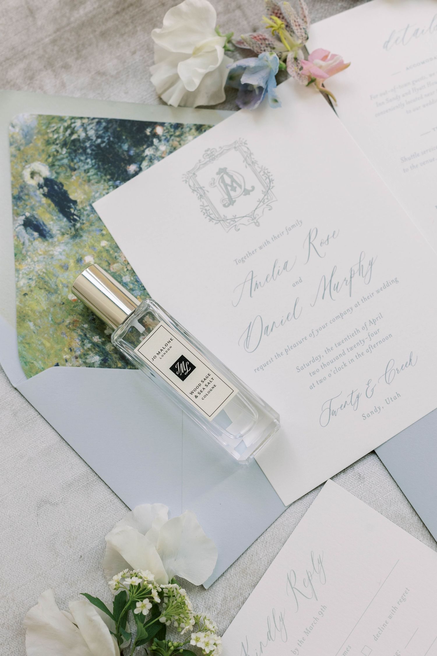 Wedding invitation suite with perfume bottle and floral accents on light blue background.
