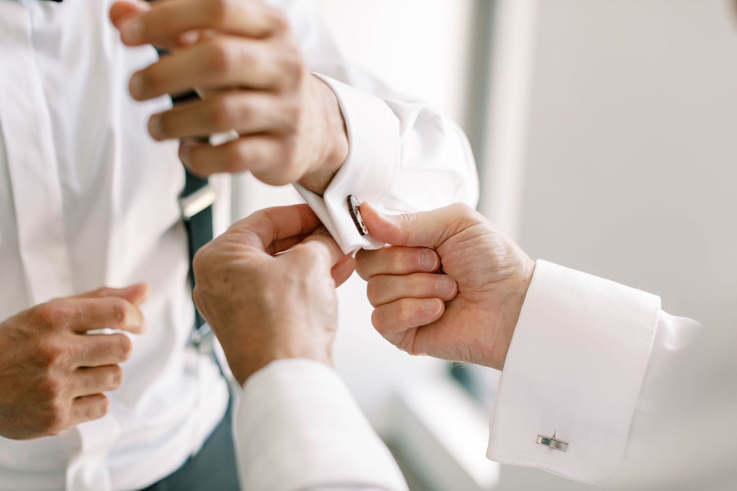 Close-up of hands fastening cufflinks on white dress shirt sleeves.