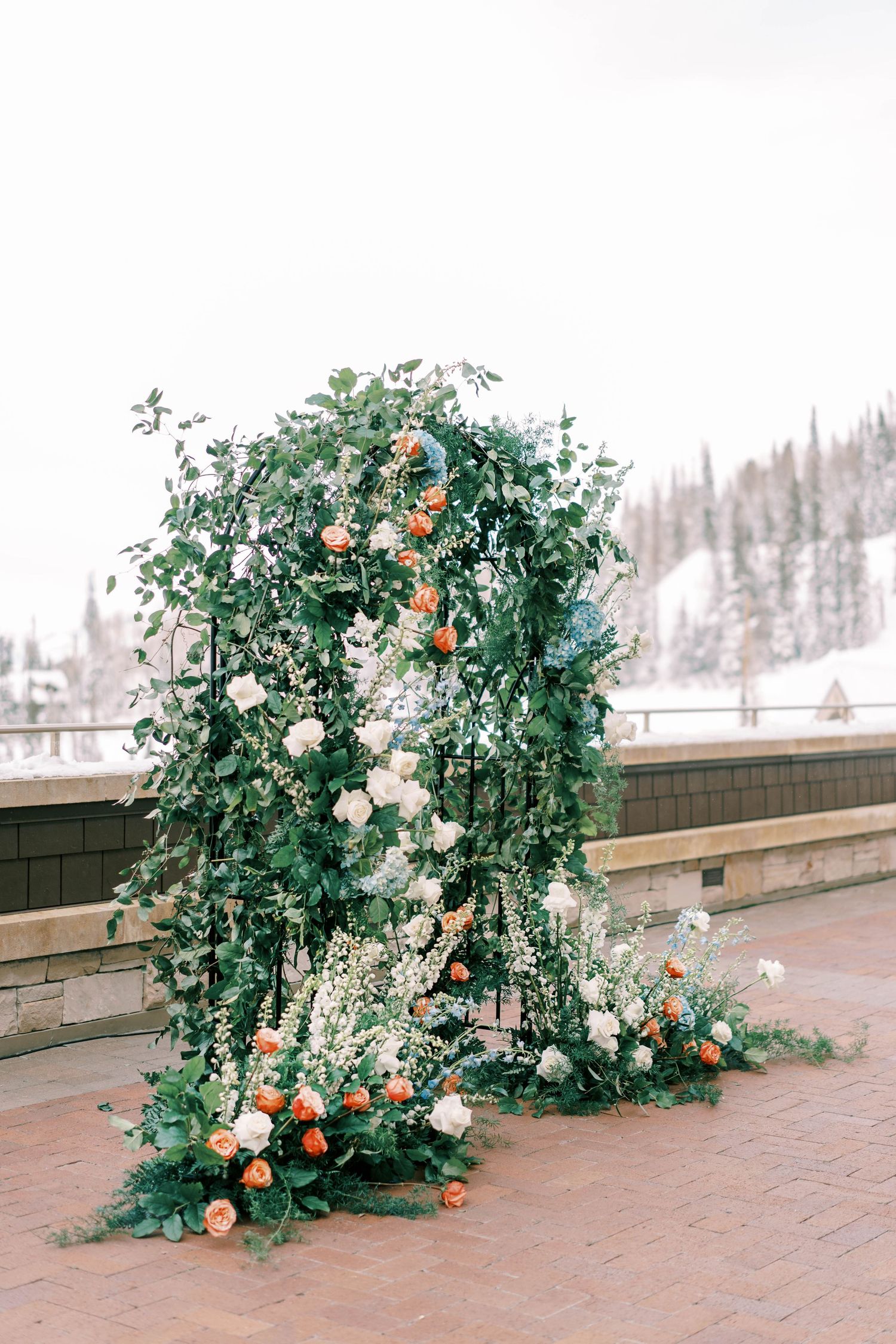 Ornate wedding arch decorated with lush greenery, white and peach roses against a winter mountain backdrop at the montage deer valley.