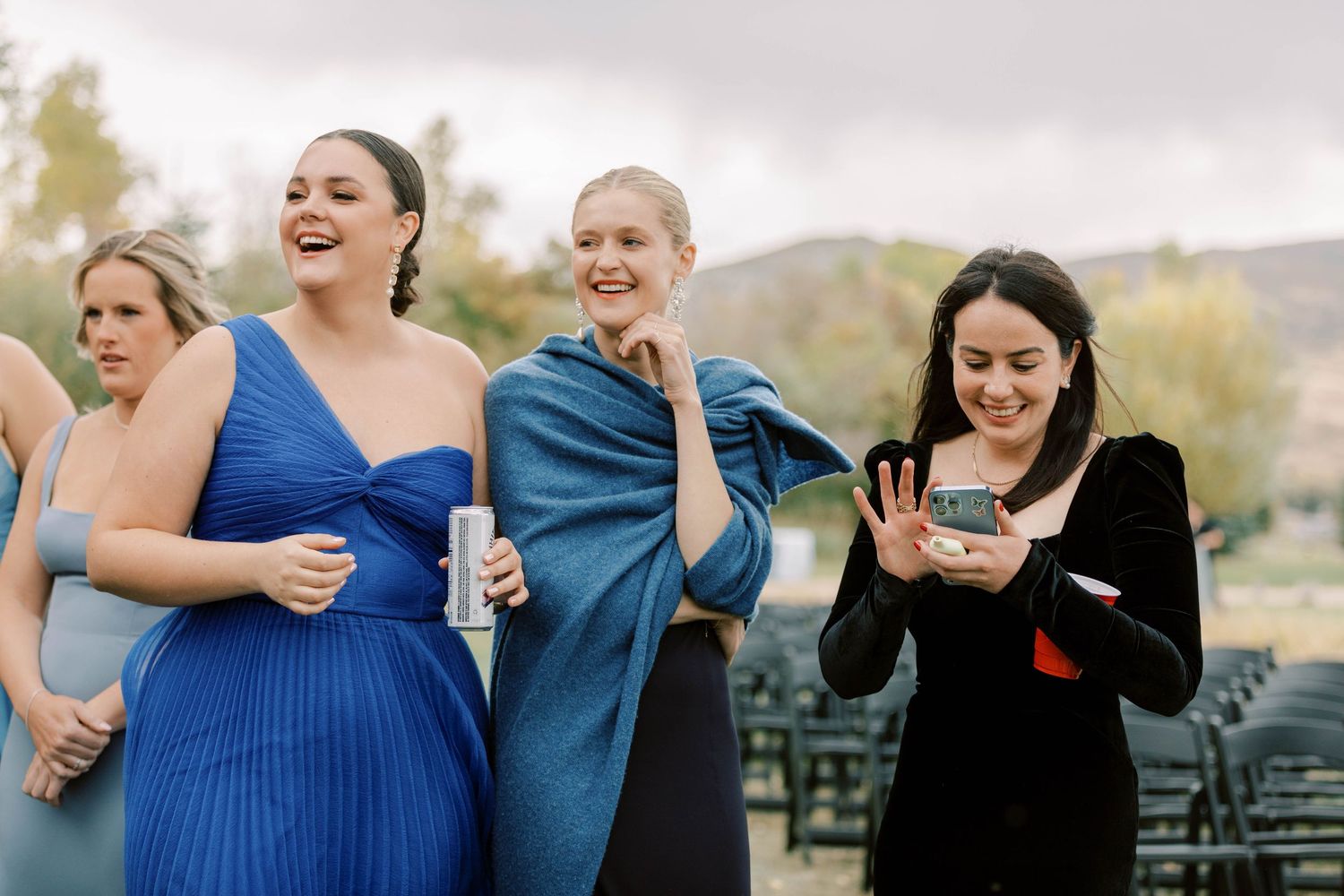 Wedding guests in blue and black dresses share a joyful moment outdoors.