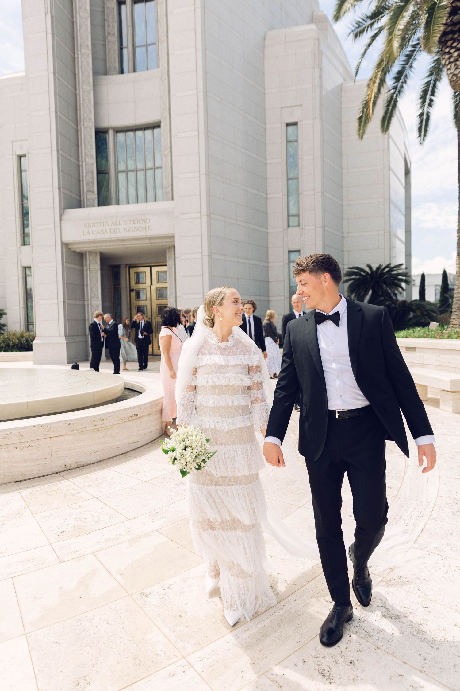 Wedding couple walking outside white temple building with palm trees at rome italy lds temple.
