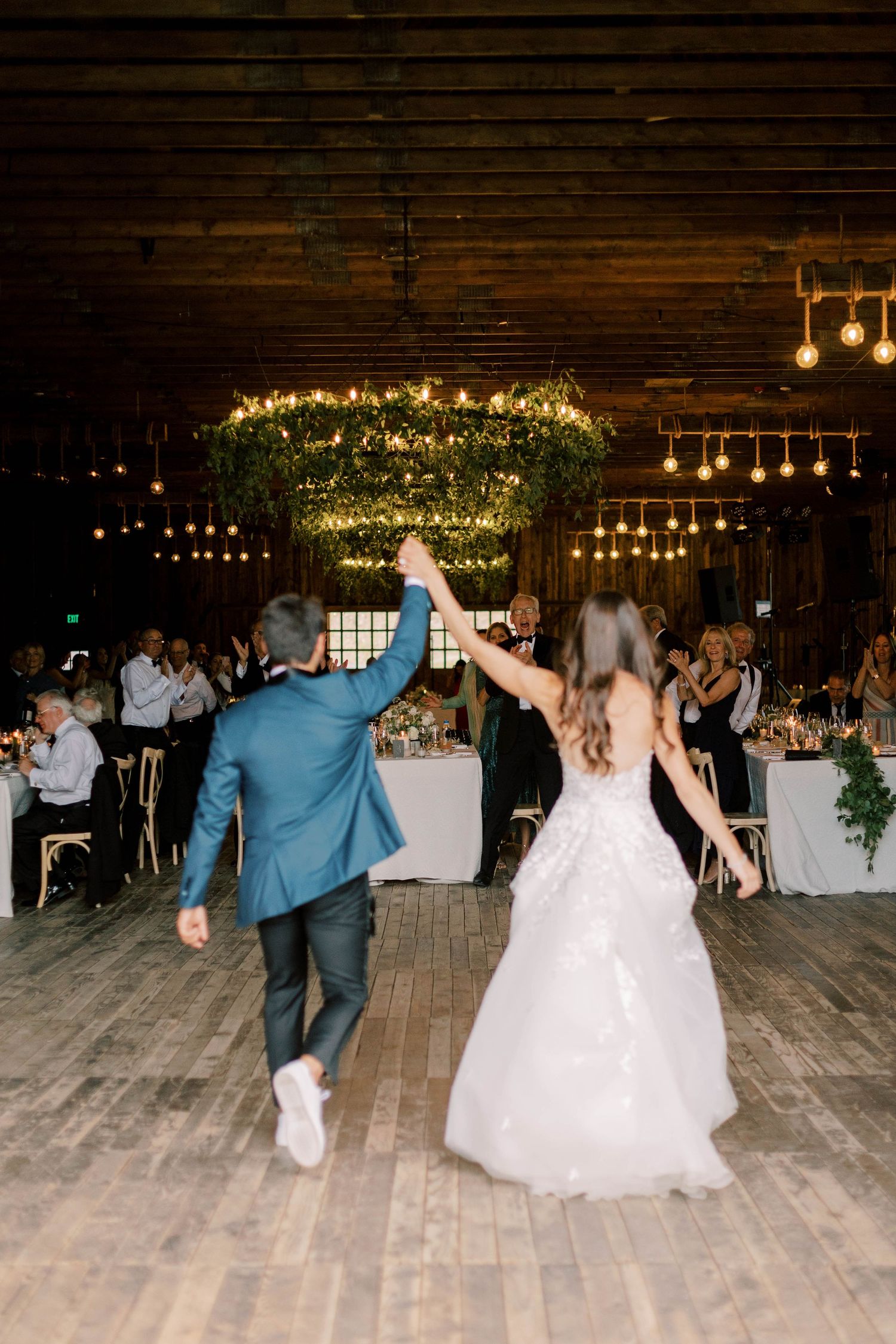 A couple enters their reception venue beneath twinkling lights and greenery chandeliers.