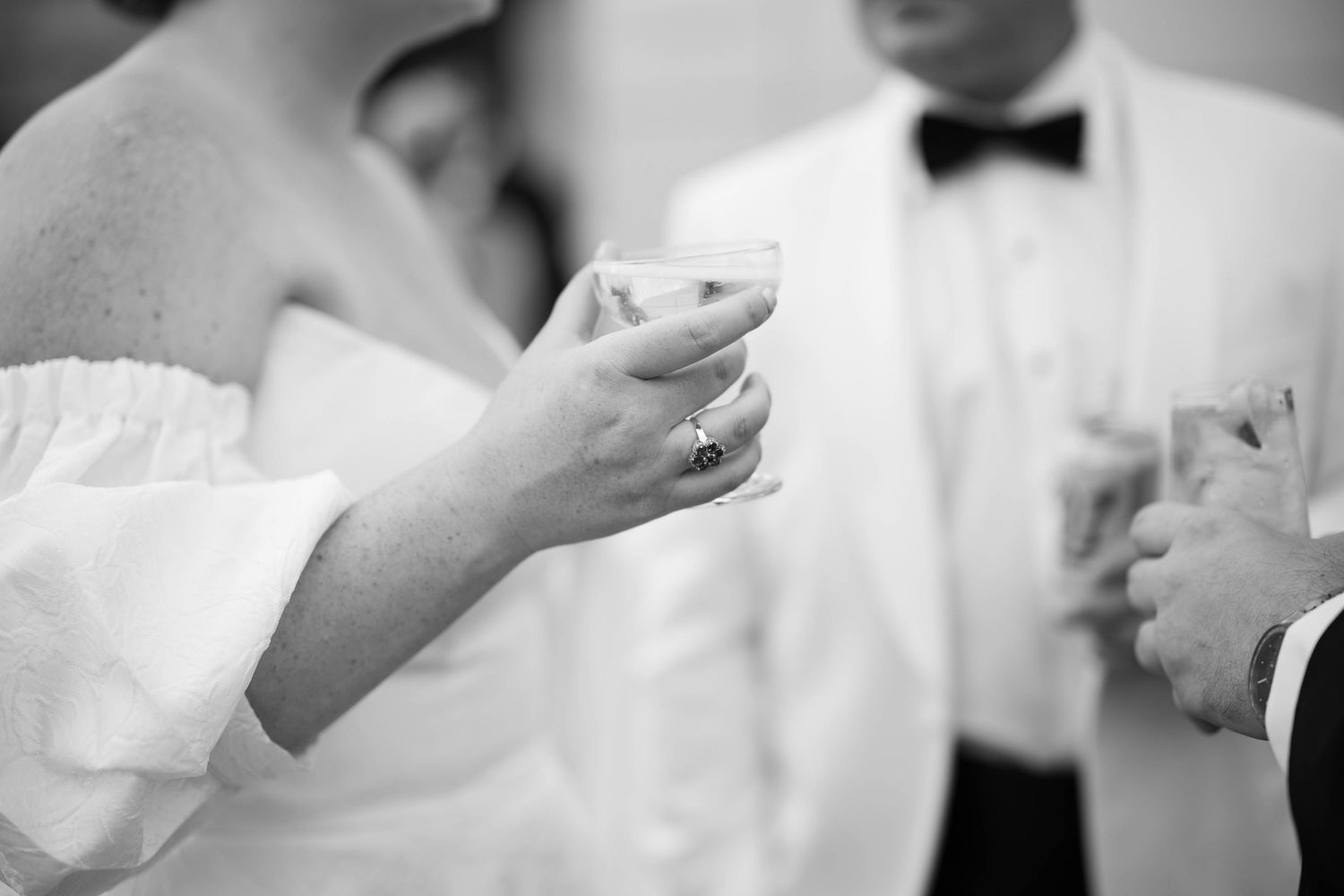 Black and white detail shot of hands holding cocktail glasses at a formal event.
