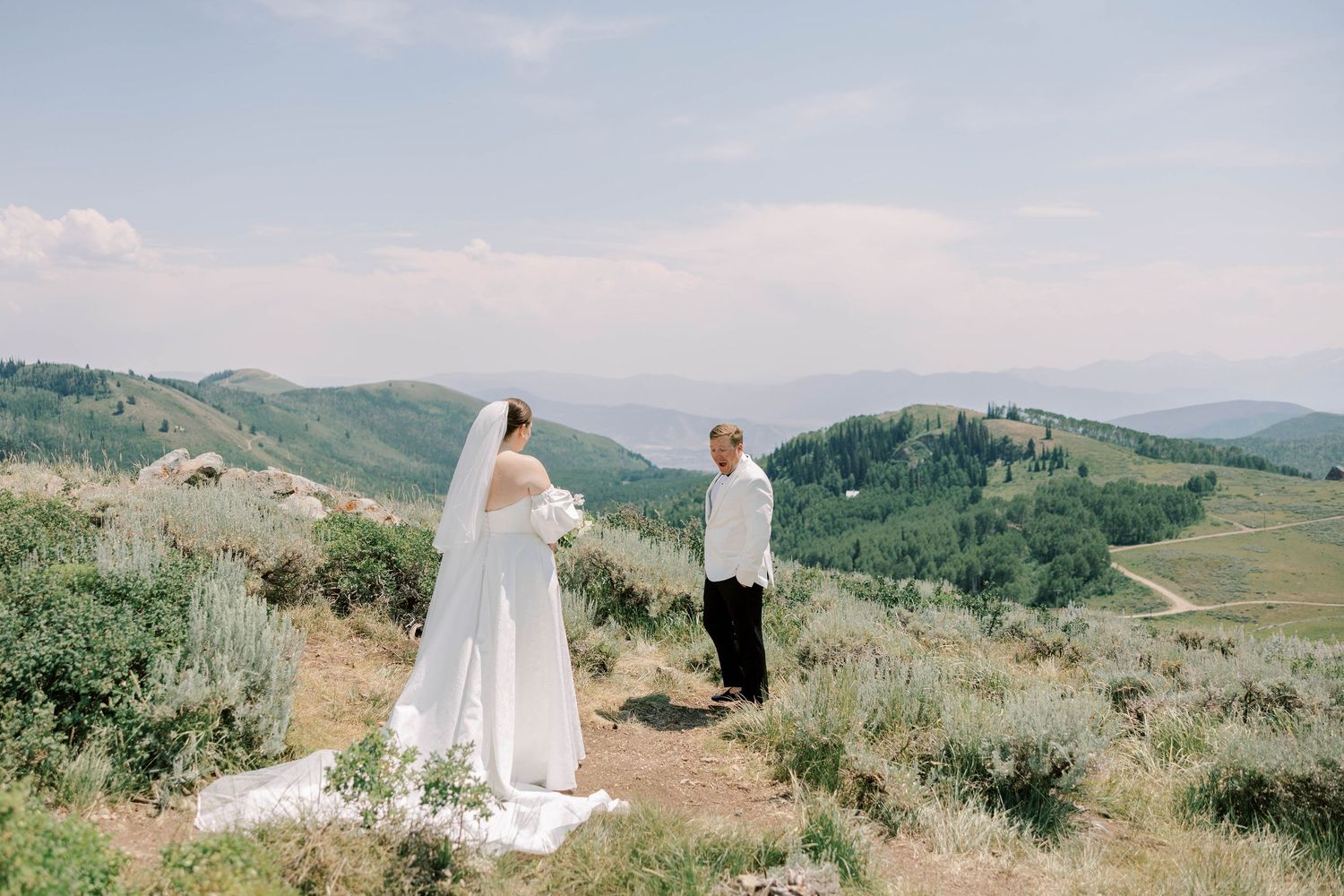 Bride and groom share a moment on hilltop with mountain landscape in background.