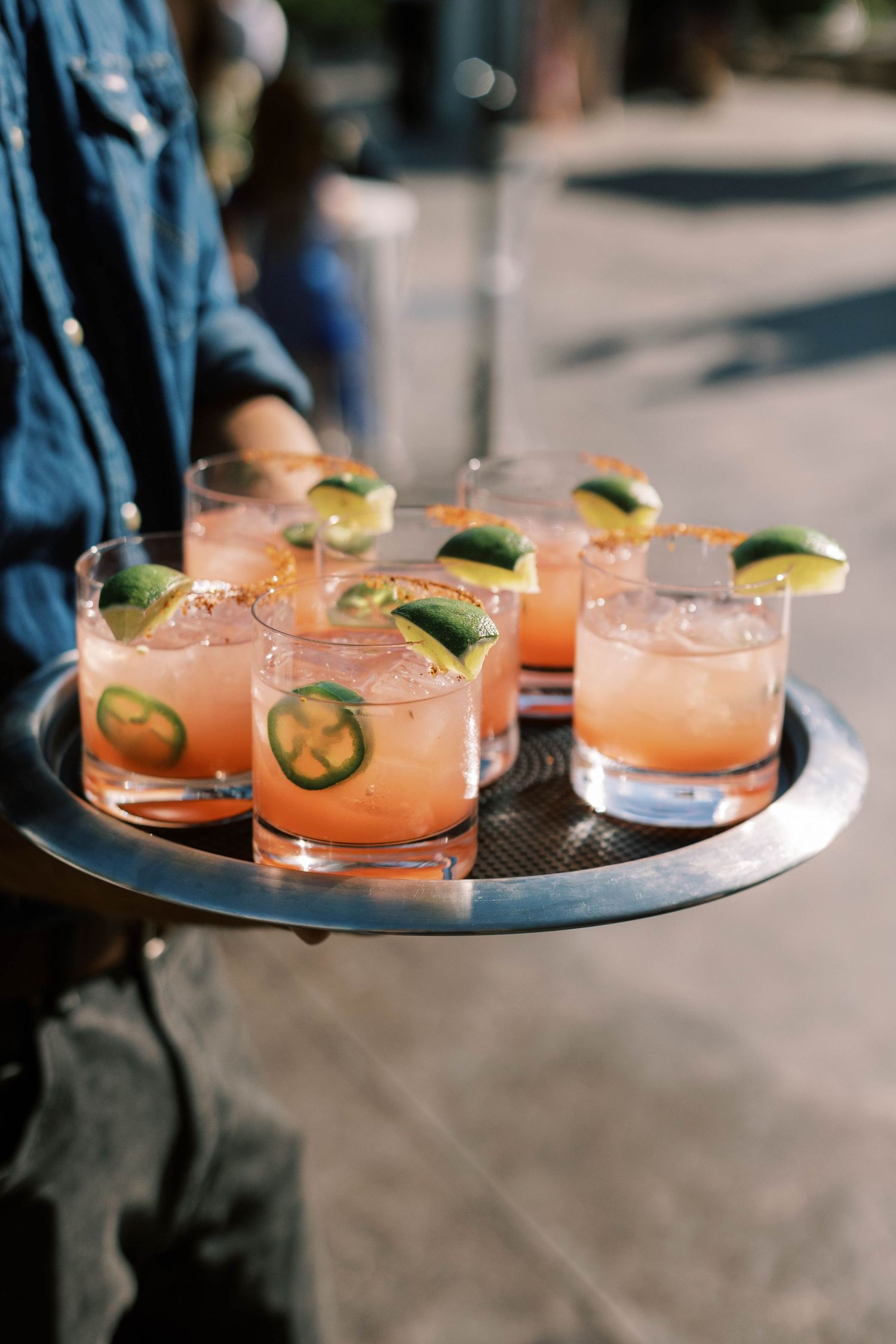 Tray of pink cocktails garnished with lime wedges and jalapeno slices being served.