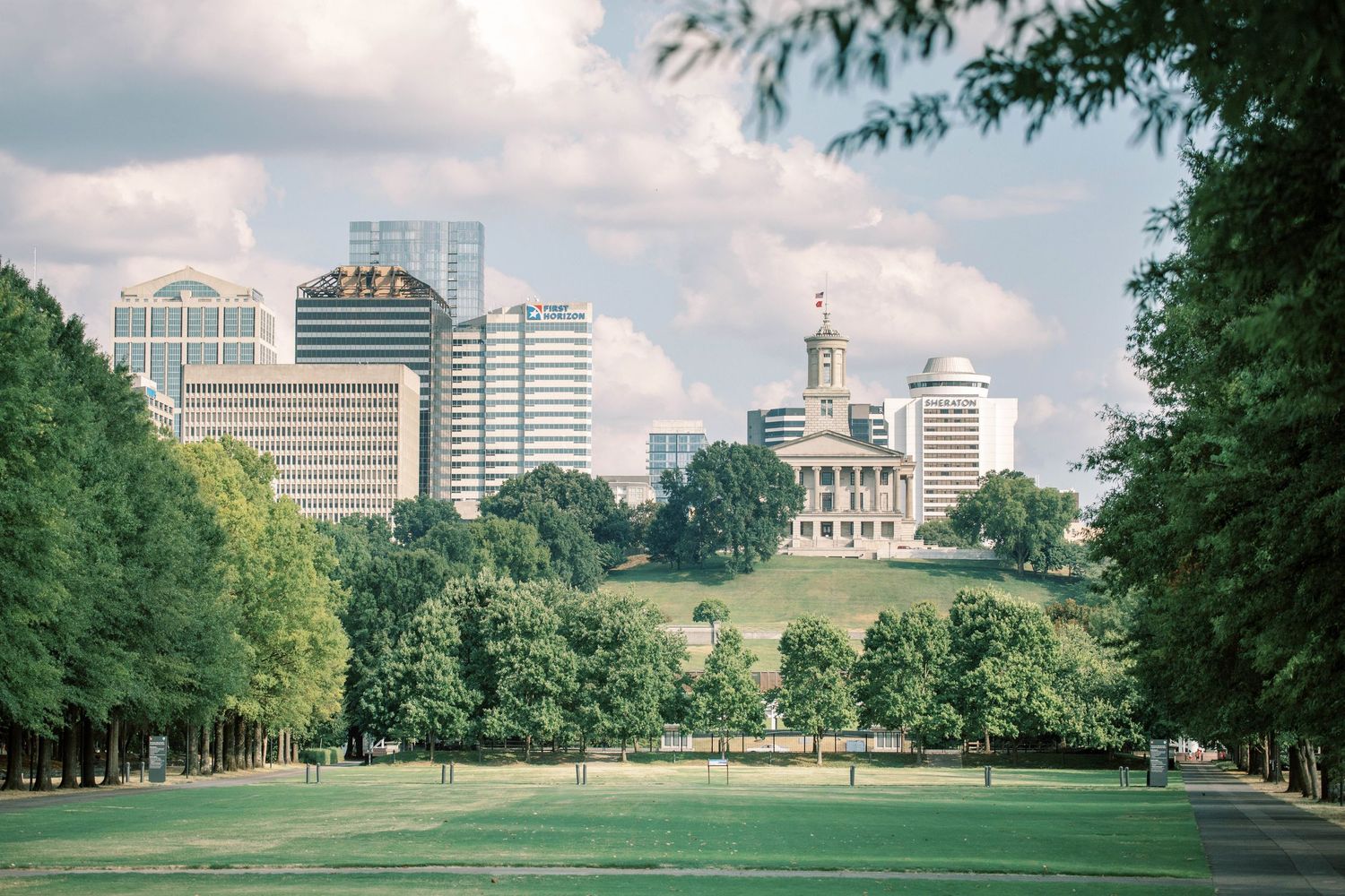 Nashville skyline view with State Capitol building and downtown buildings visible through trees.