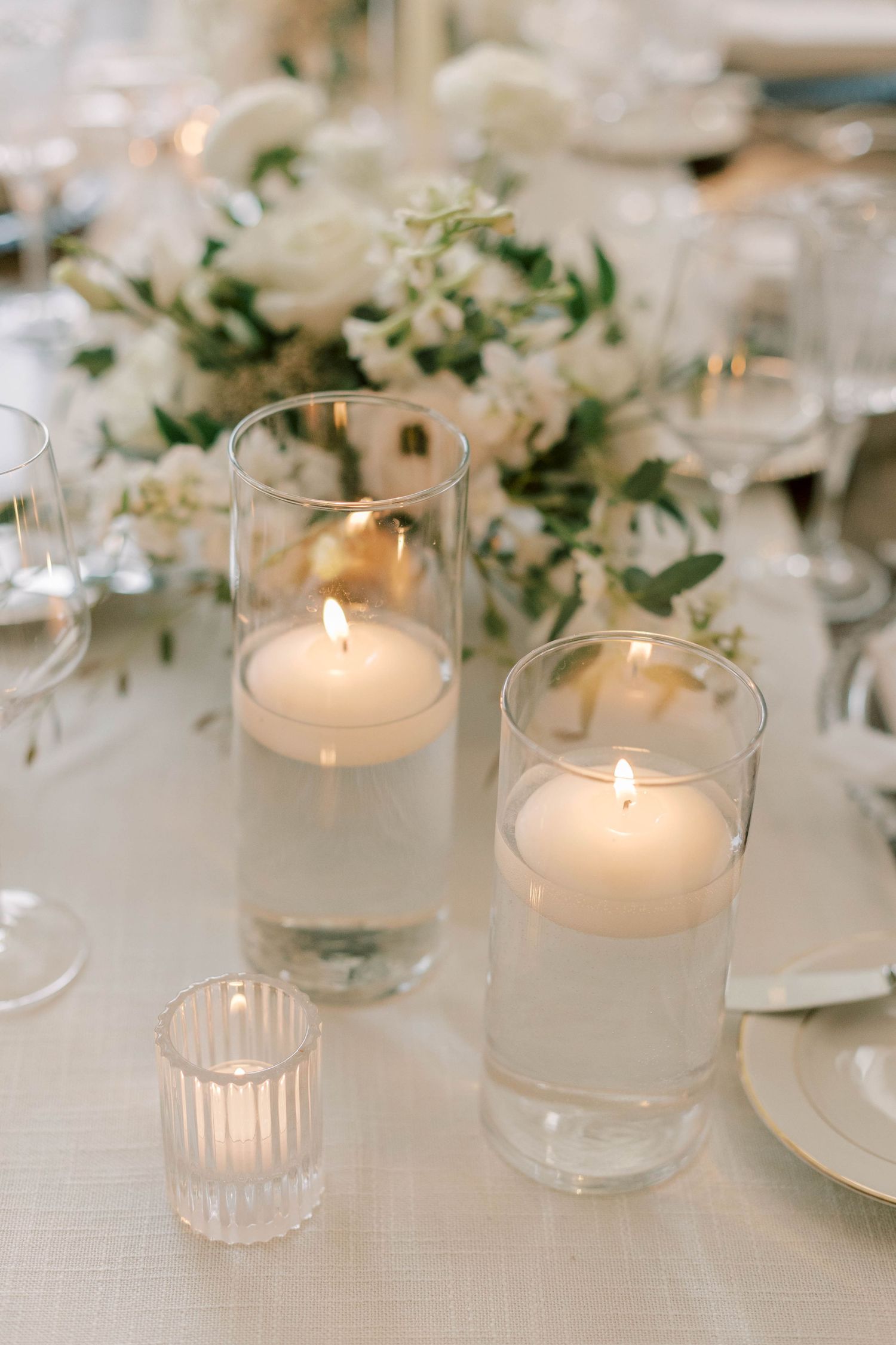 White floating candles in glass cylinders with delicate floral arrangements on a wedding table.
