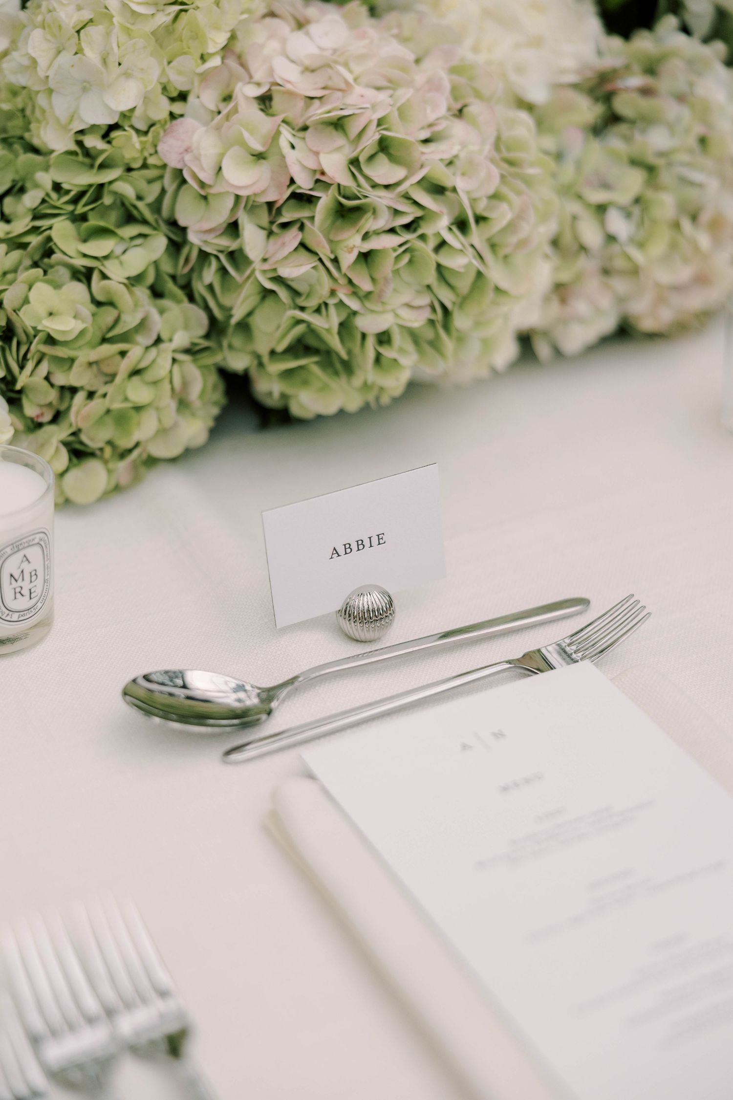 Place setting with white hydrangeas and silverware on crisp white tablecloth.