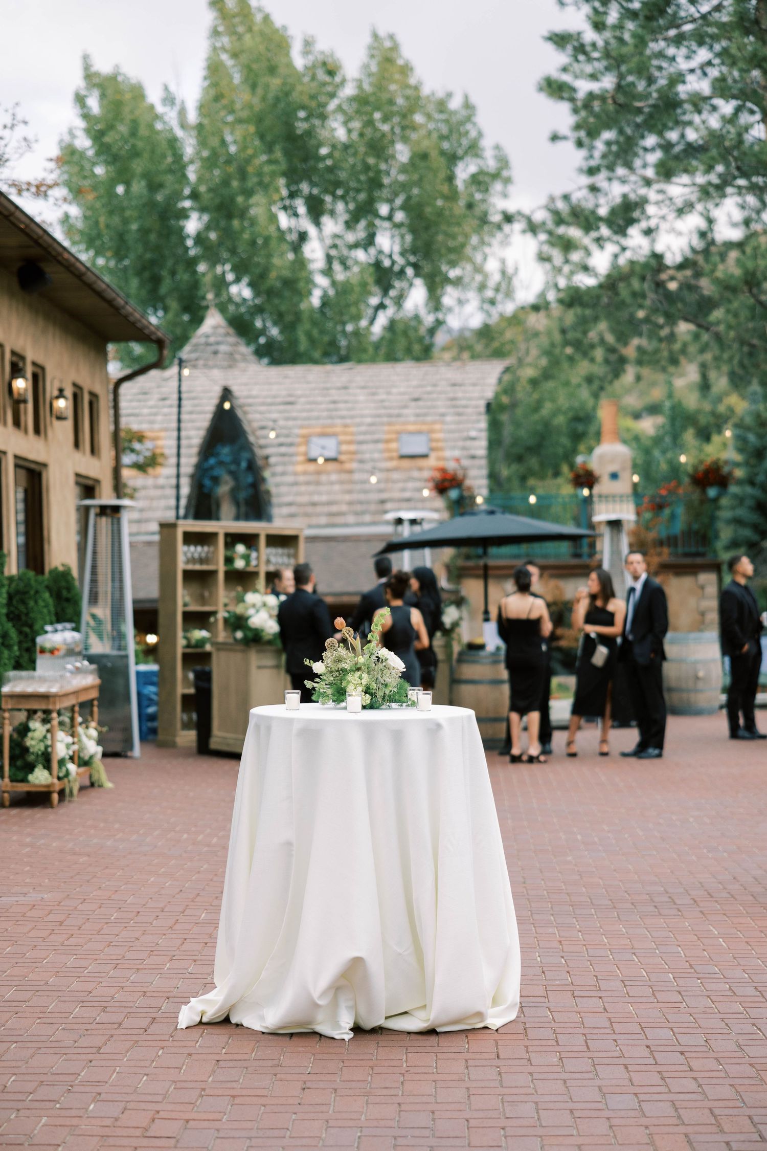 Elegant cocktail reception setup with white tablecloth and guests mingling in background.