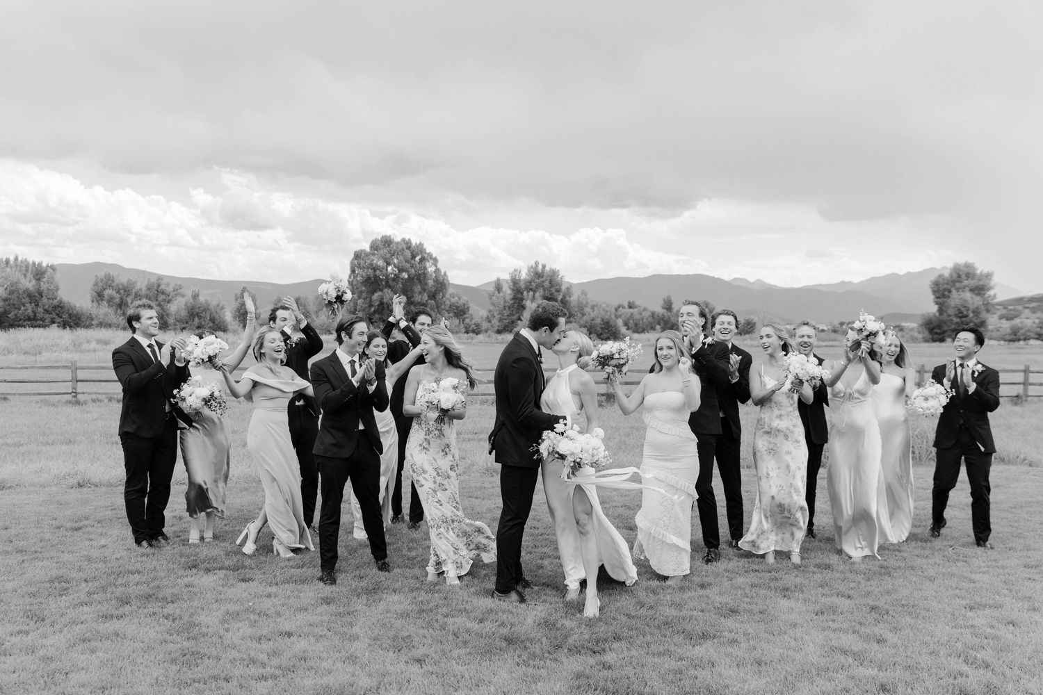 Black and white photo of wedding party gathered in a circle outdoors.