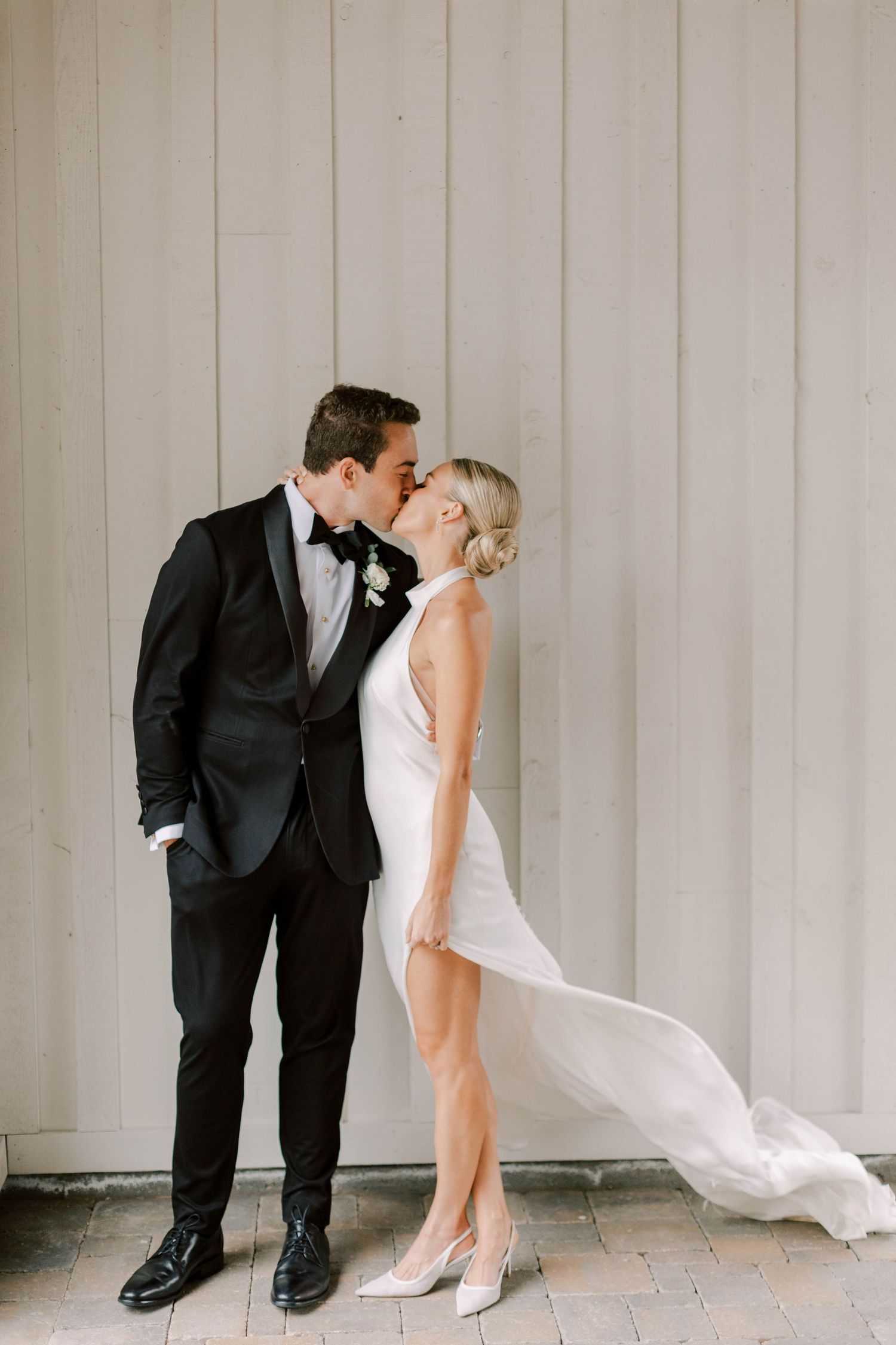 Elegant couple shares romantic moment against gray wall, bride's white dress flowing in stylish wedding photo.