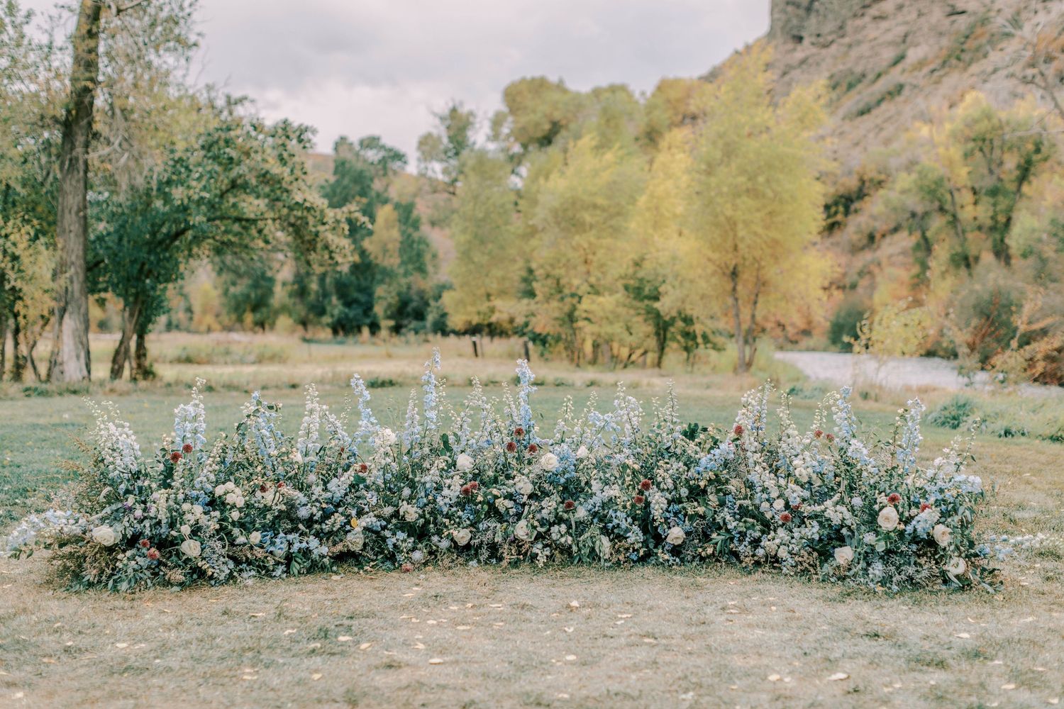 A lush floral arrangement in blue and white hues decorates an outdoor garden setting against a mountainous backdrop.