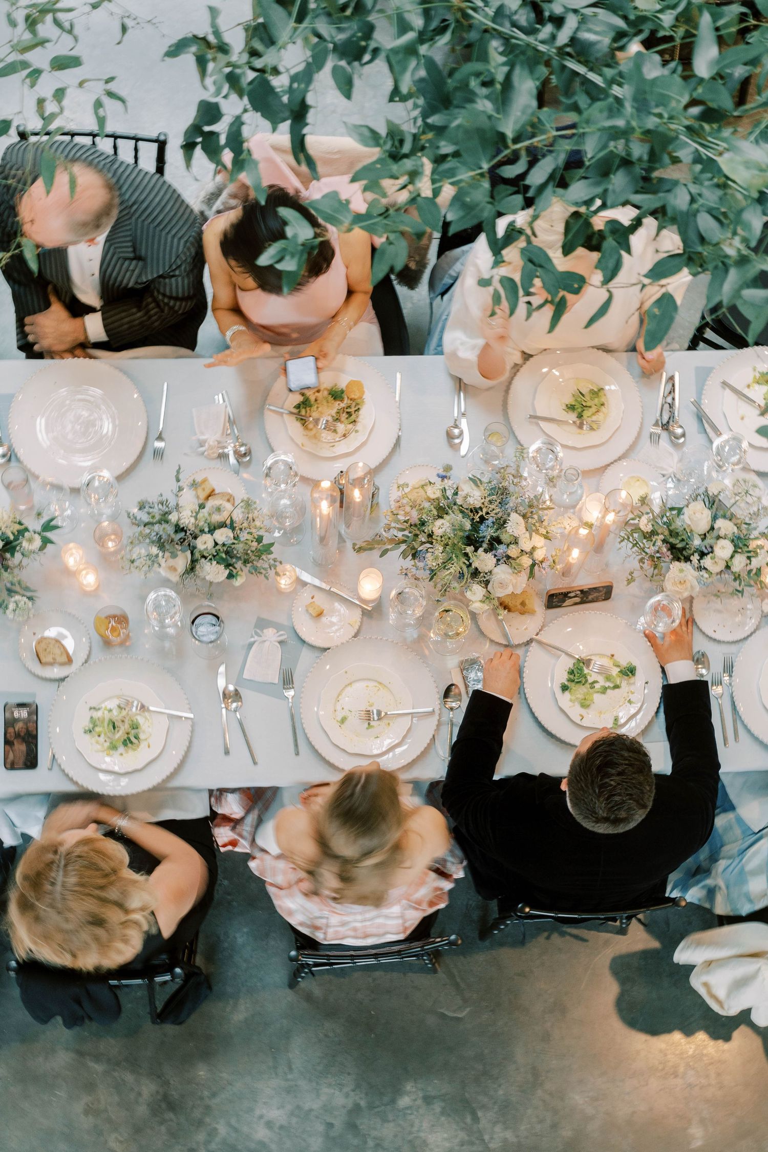 Overhead view of elegant table settings with floral centerpieces and candlelight during a dinner event.
