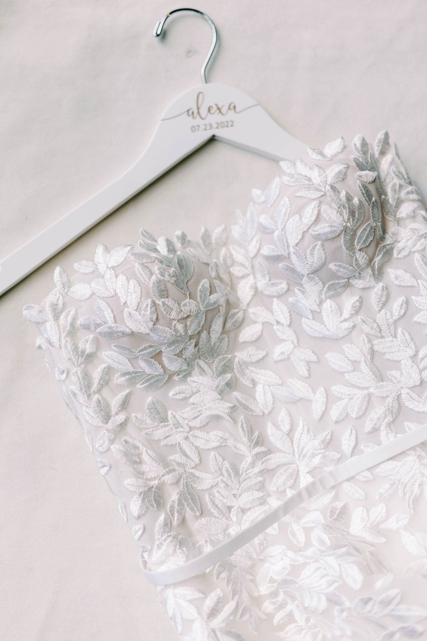 Close up of a delicate white lace wedding dress bodice hanging on a personalized bridal hanger.