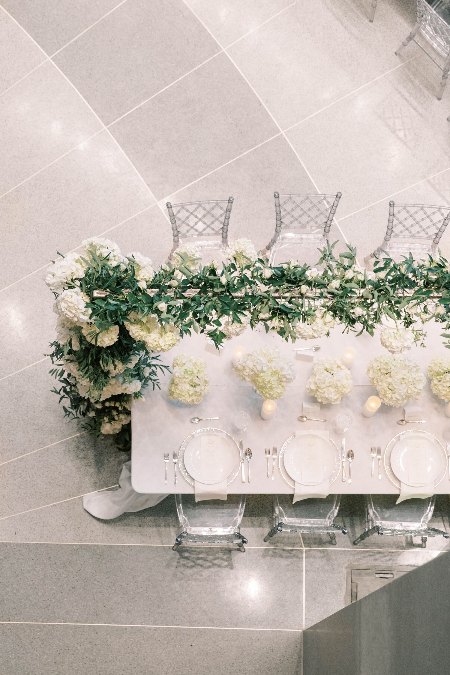 Overhead view of wedding table with ghost chairs and white floral runner.