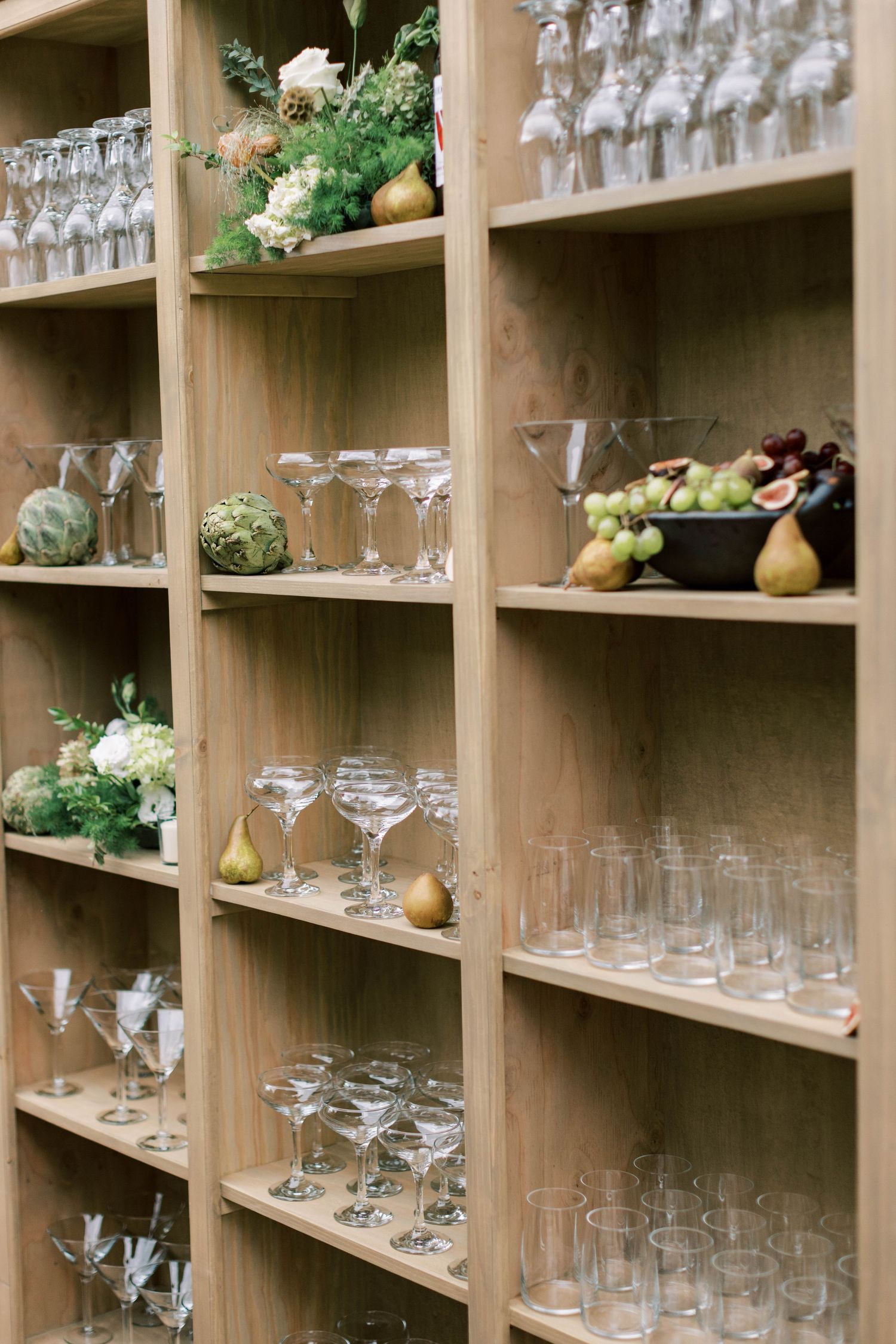 Wooden shelving displays crystal glassware and decorative pears for an elegant event setup.