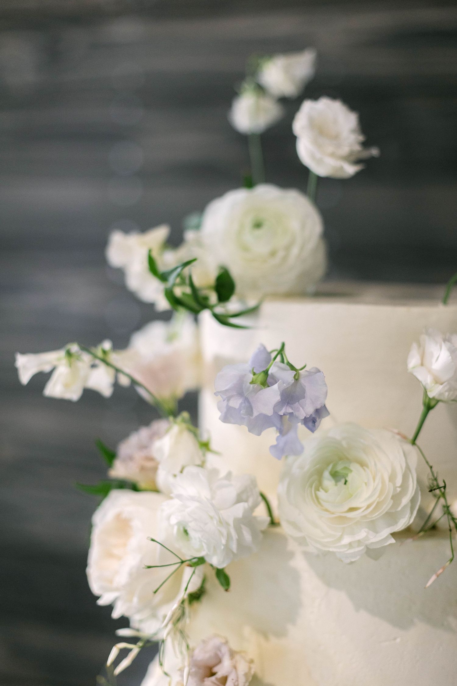Close-up of white and purple flowers decorating a wedding cake with soft bokeh background.