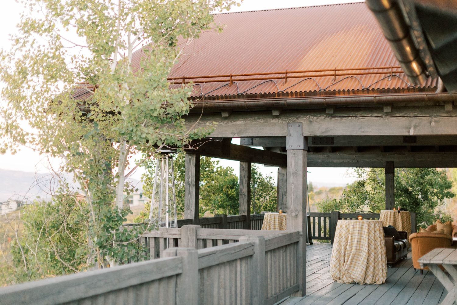 Rustic covered deck with wooden railings and draped tables overlooking a scenic landscape.