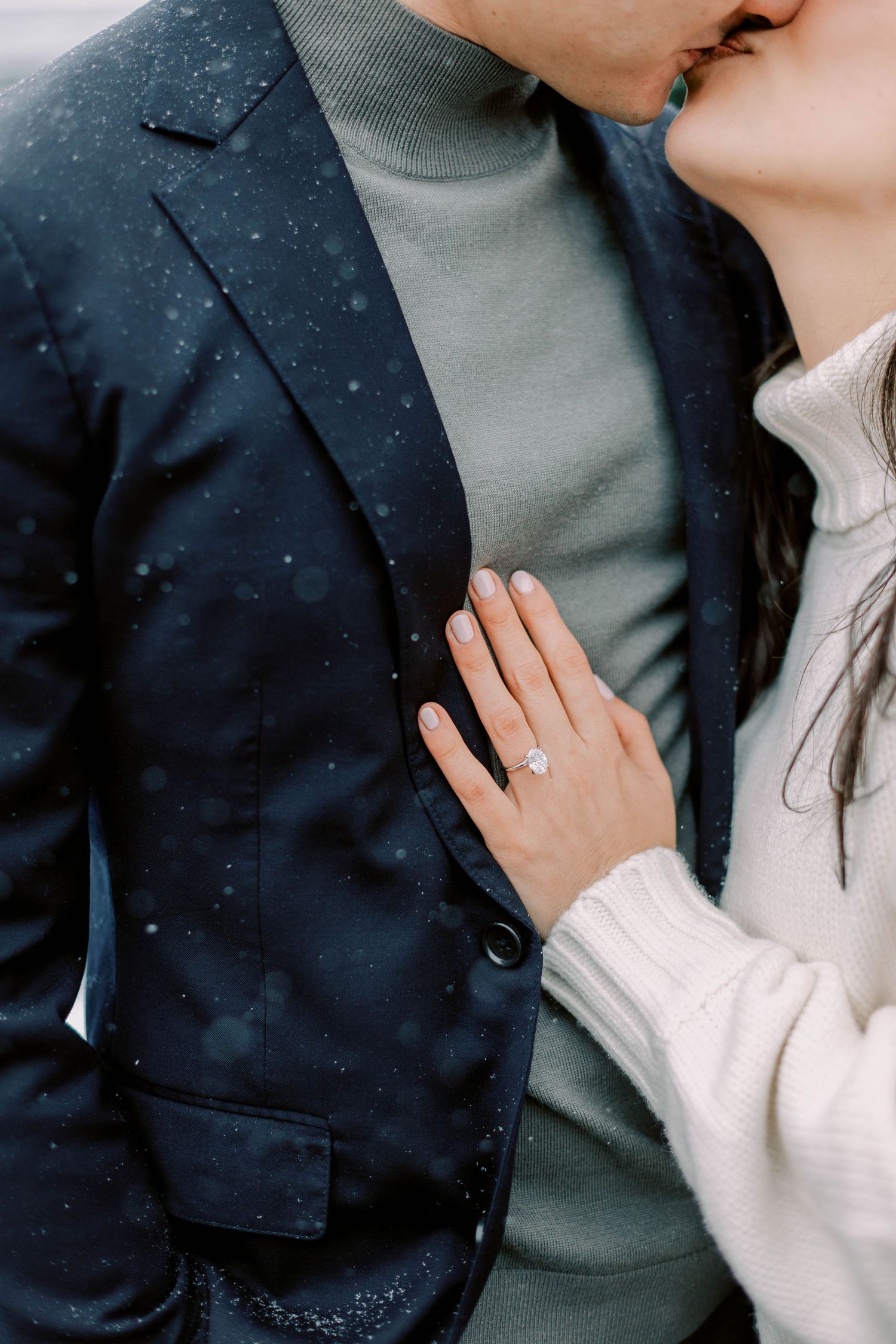 Close-up of engagement ring against navy blazer and white sweater.