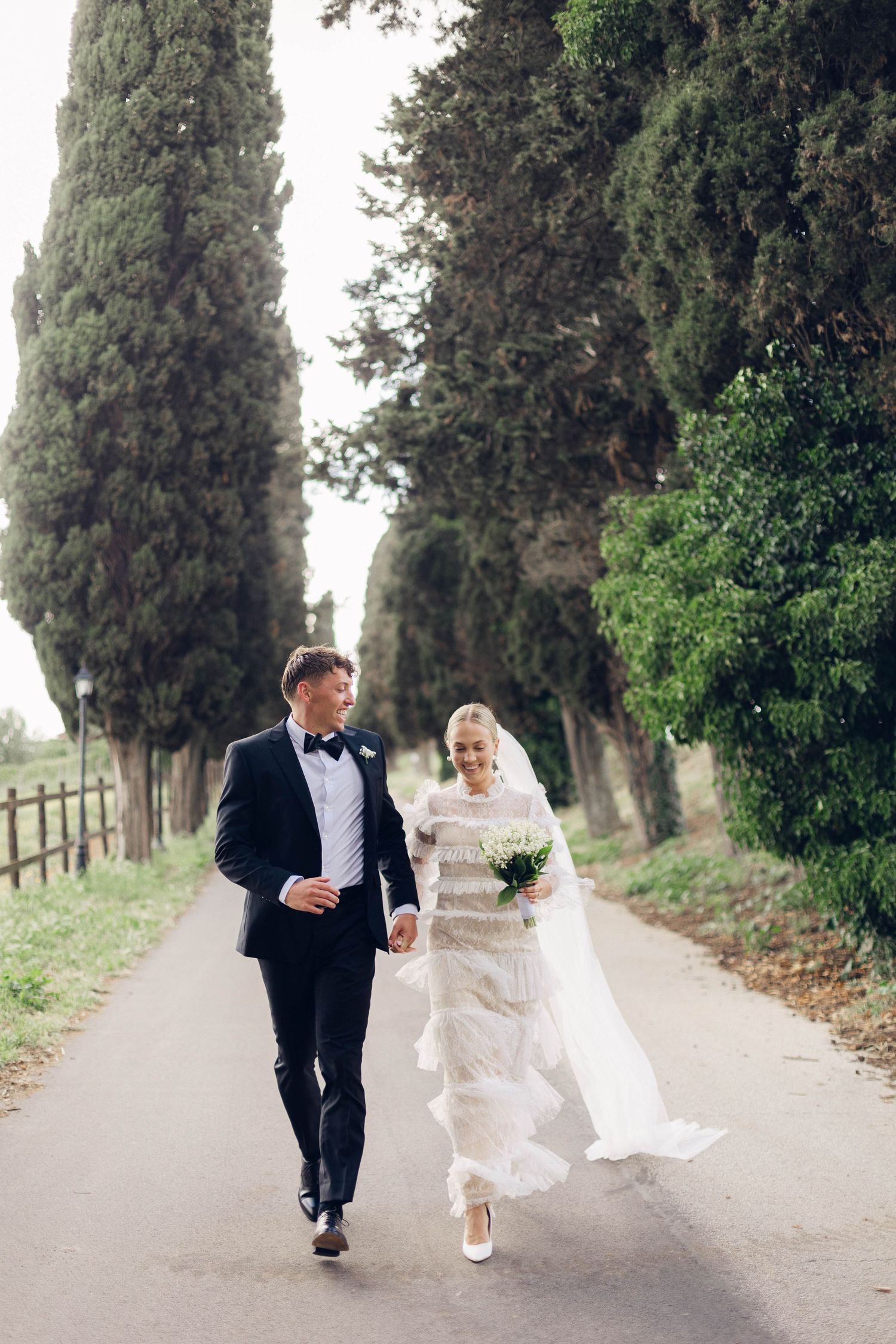 A couple strolls down a cypress tree-lined path in Italy on their wedding day at castello della castellucia in rome.