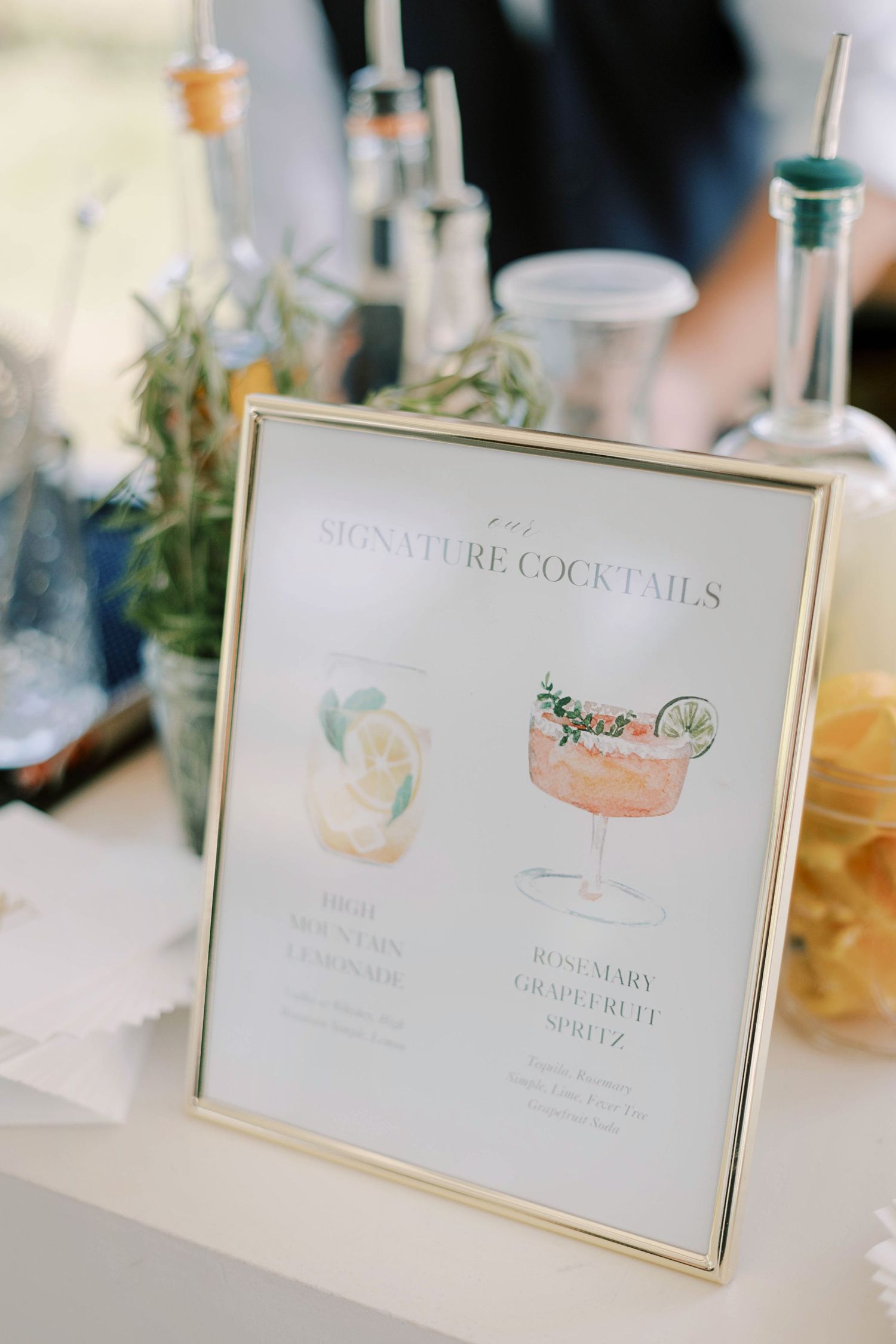 Framed menu displaying watercolor illustrations of signature cocktails in gold frame.