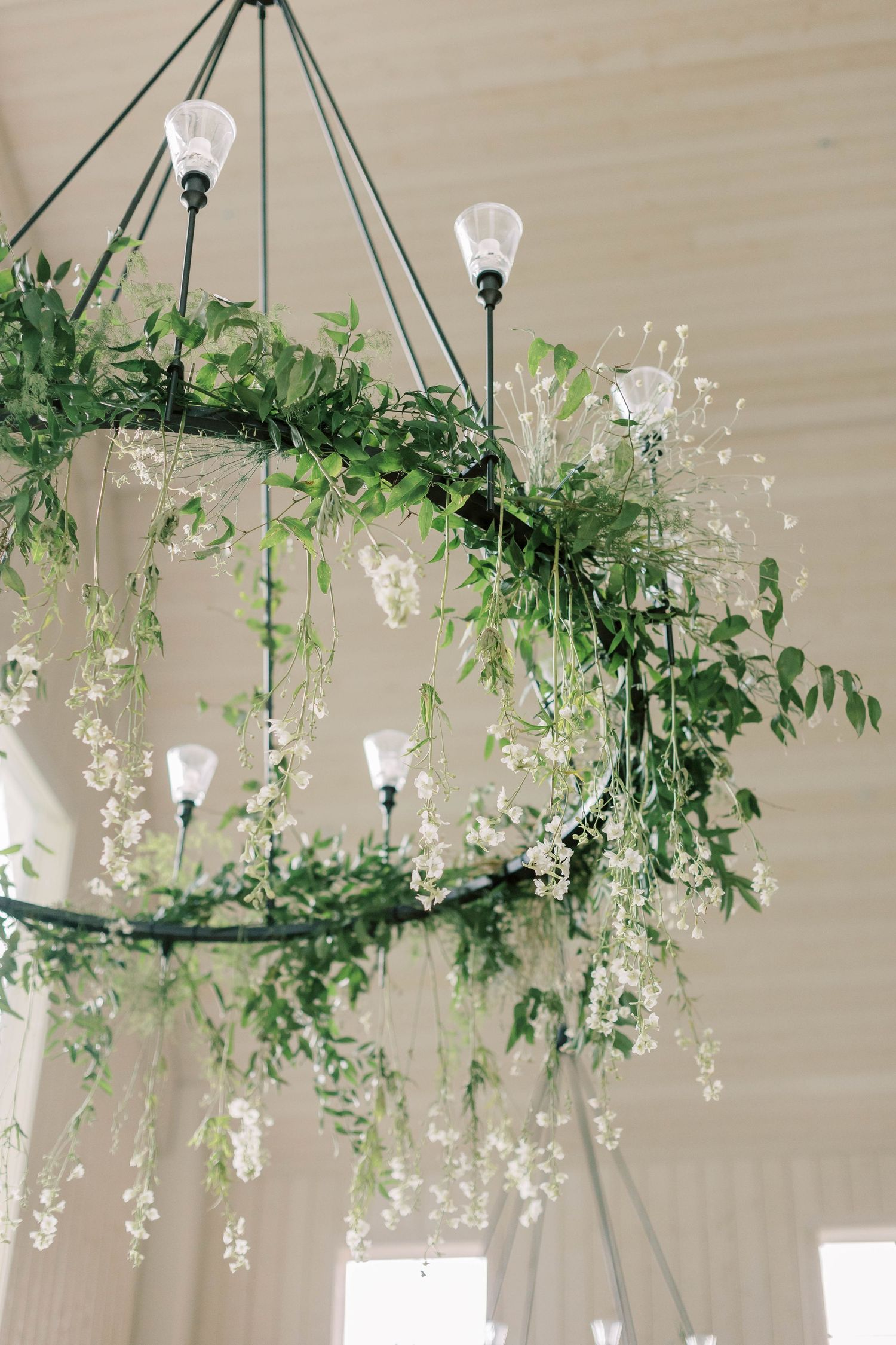 Elegant chandelier decorated with cascading greenery and delicate white flowers in a wedding venue setting.