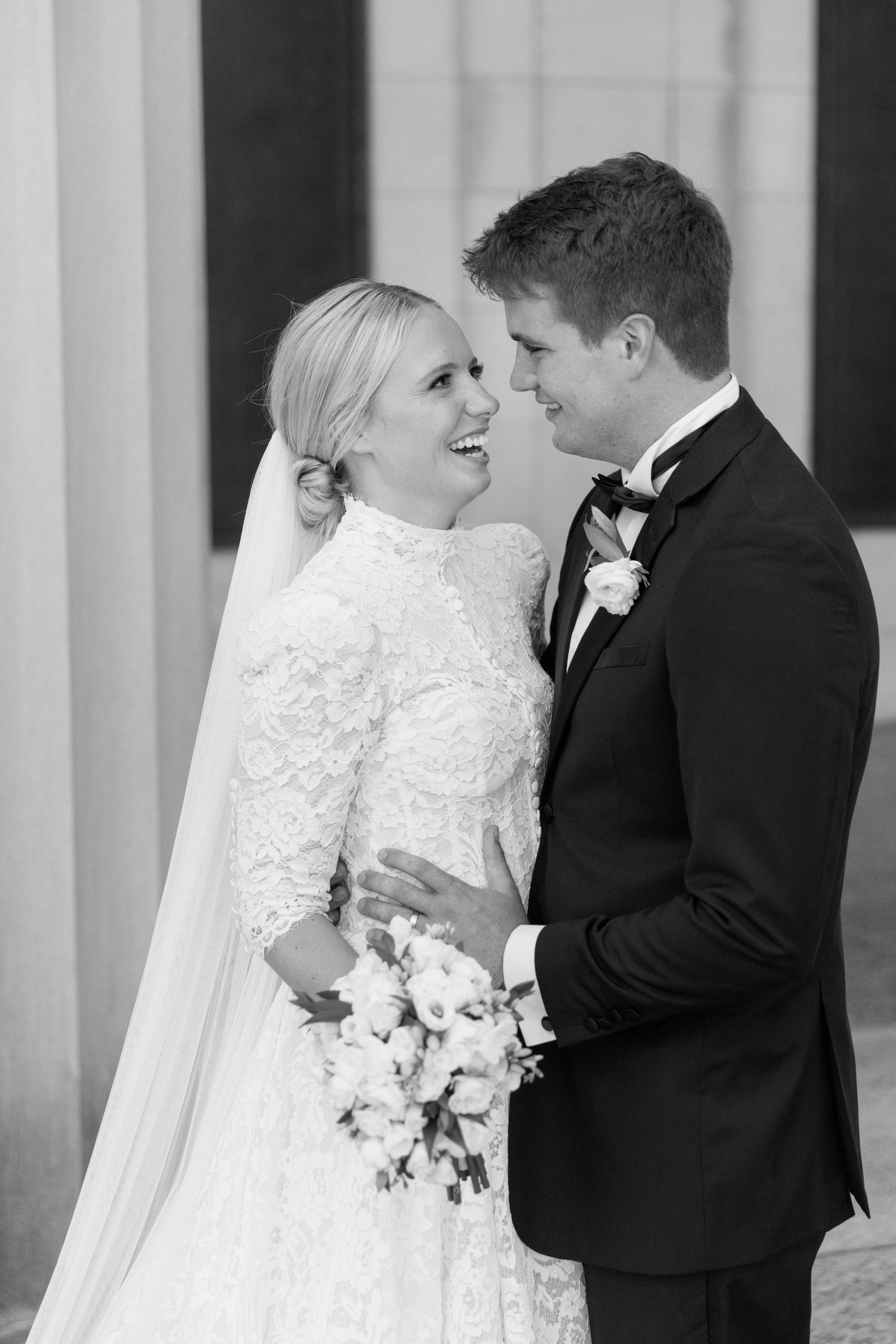 Black and white portrait of newlyweds sharing intimate moment in formal wedding attire.
